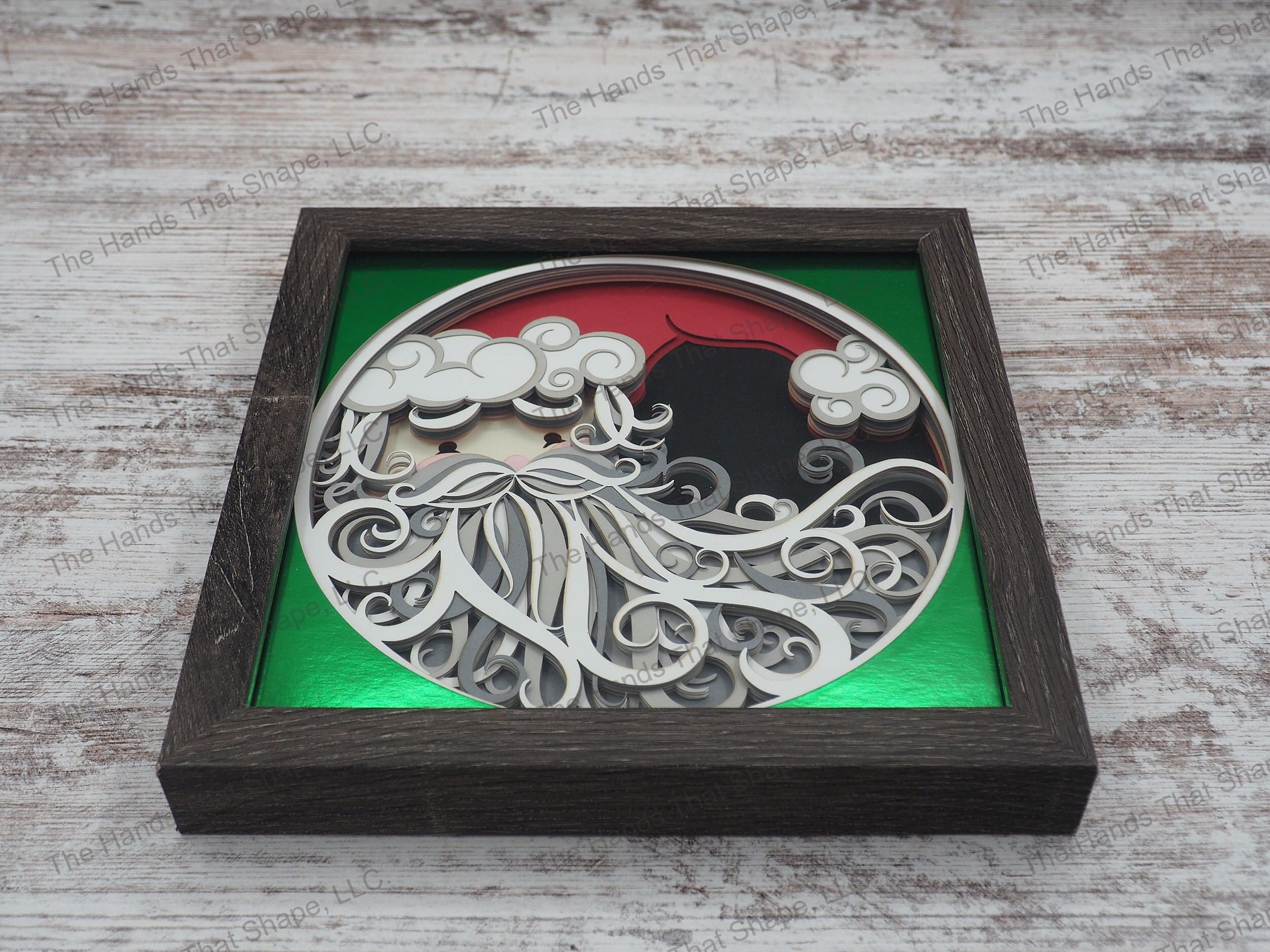 The layered paper shadow box features Santa's face with his big bushy beard, red cap and rosy cheeks.