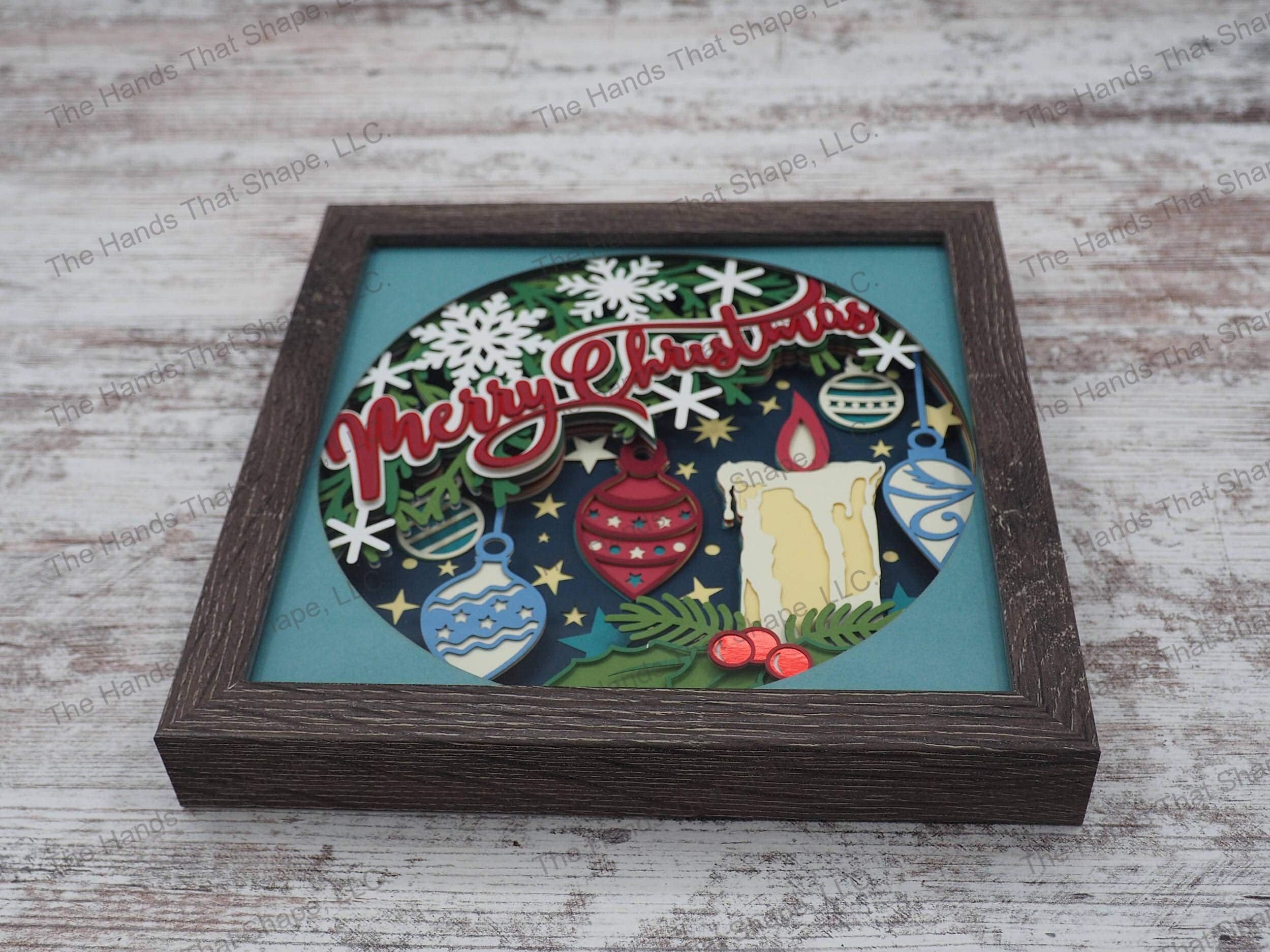 The shadow box features Christmas tree in the background full of ornaments, holly, berries, snowflakes and a Christmas Candle burning brightly with the words "Merry Christmas" dancing across the tree.