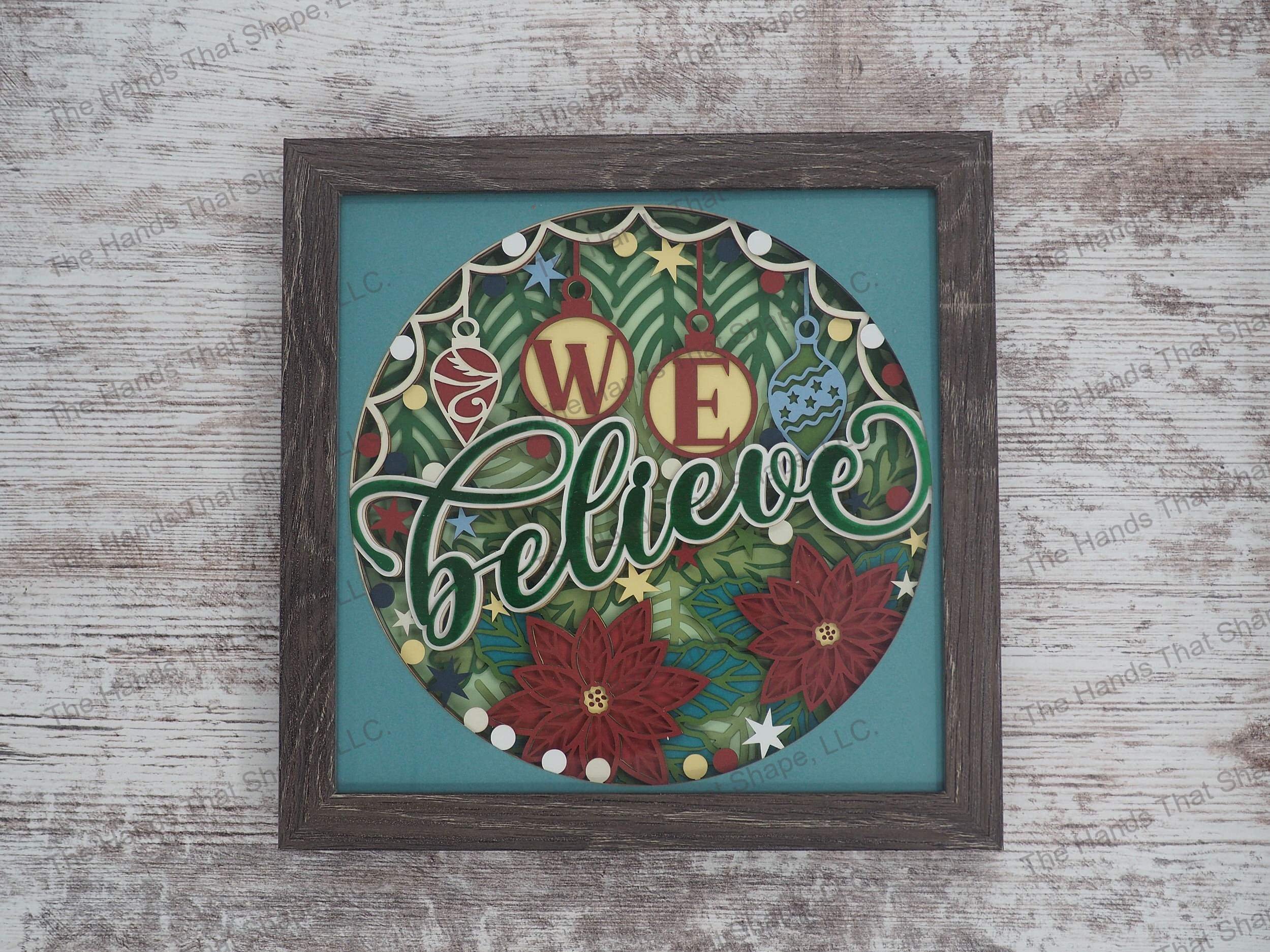The shadow box features a Christmas tree in the background full of ornaments and poinsettias with the words "We Believe" in the foreground.