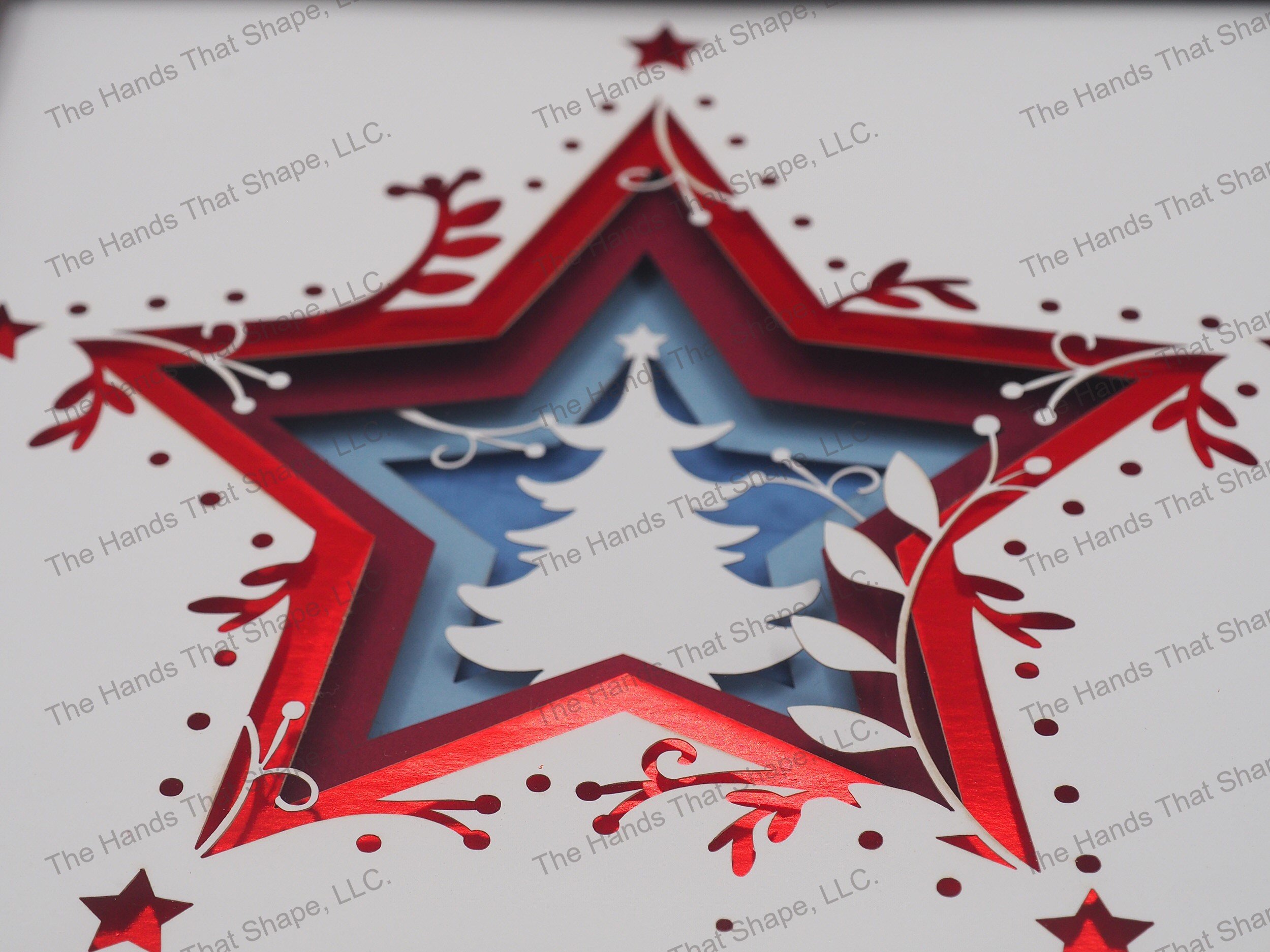 The shadow box features layers of cardstock paper to create a 3d Christmas Tree in the center of a multi-layer stacked star.