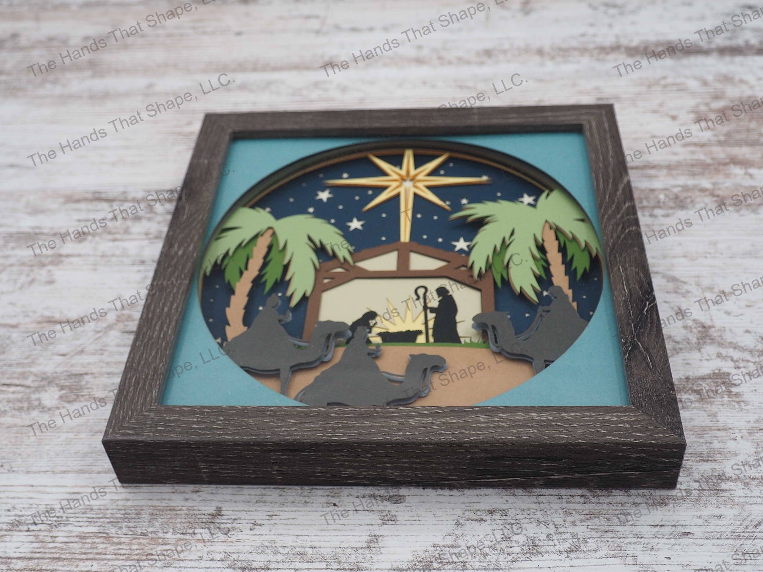 The shadow box features layers of cardstock paper to create a 3d nativity, three wise men with the Star of Bethlehem high overhead.
