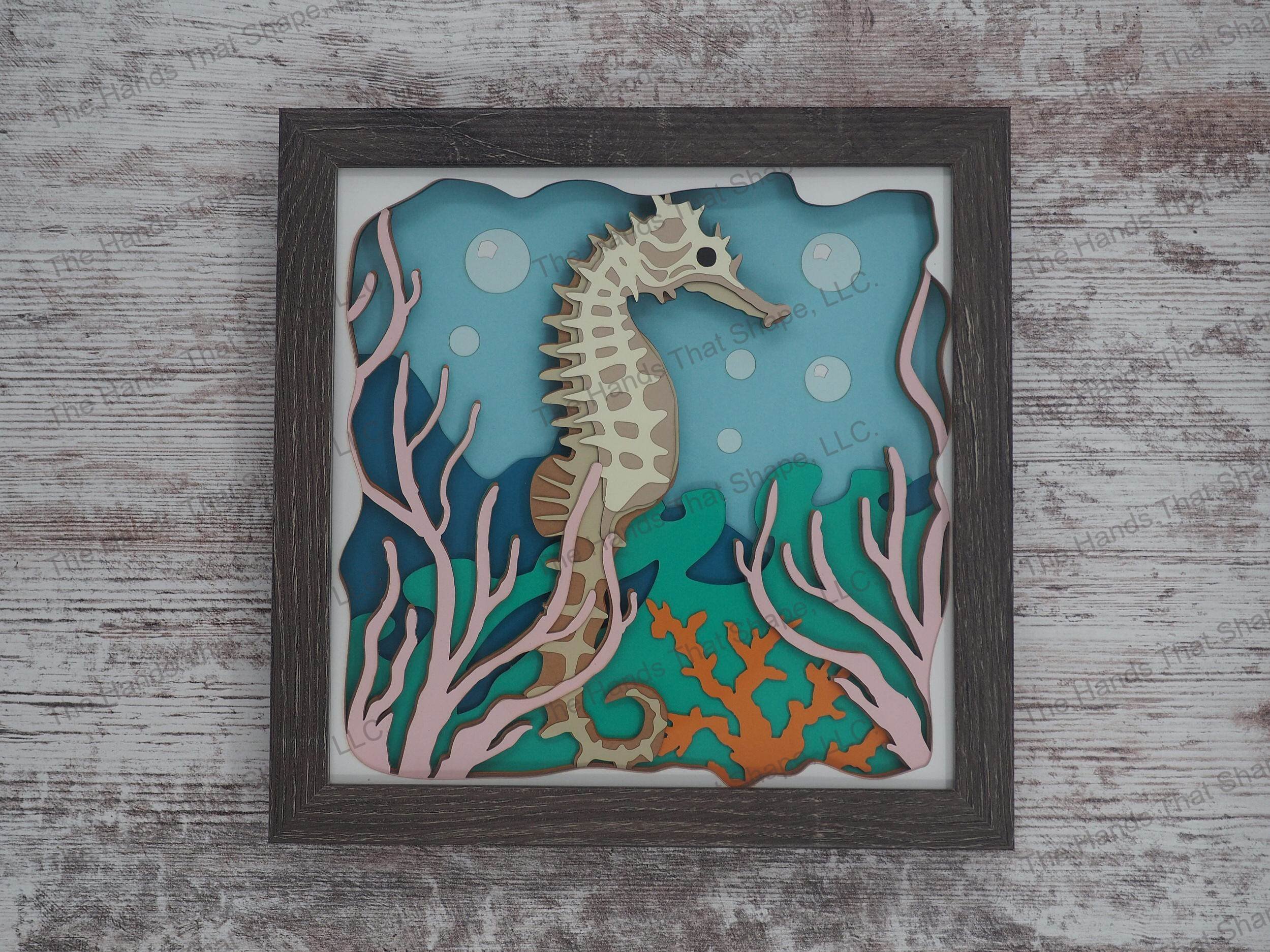 The shadow box features layers of cardstock paper to create a 3d picture of a seahorse hiding among the seagrass and coral reefs.