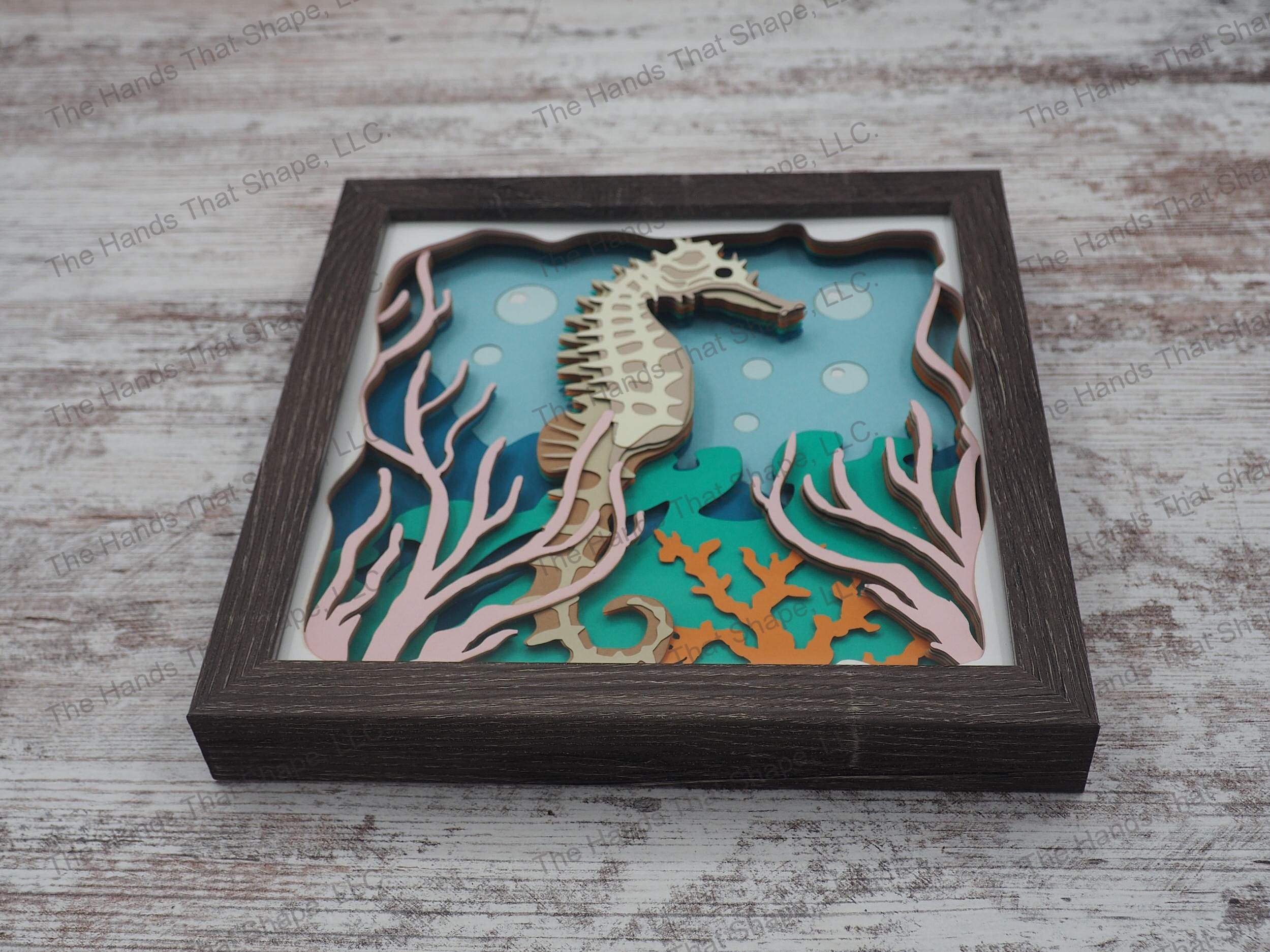 The shadow box features layers of cardstock paper to create a 3d picture of a seahorse hiding among the seagrass and coral reefs.
