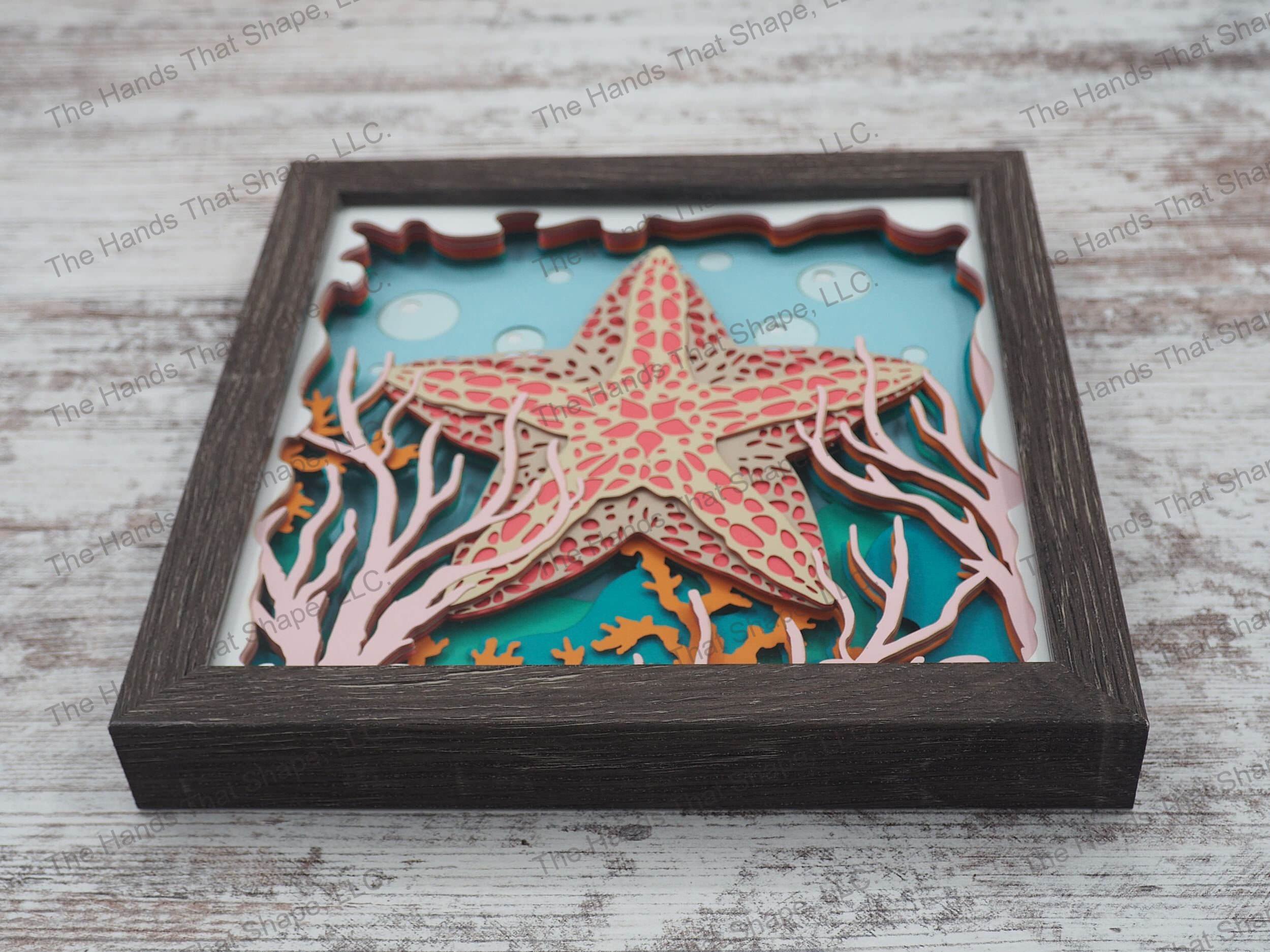 The shadow box features layers of cardstock paper to create a 3d picture of a starfish hiding among the seagrass and coral reefs.
