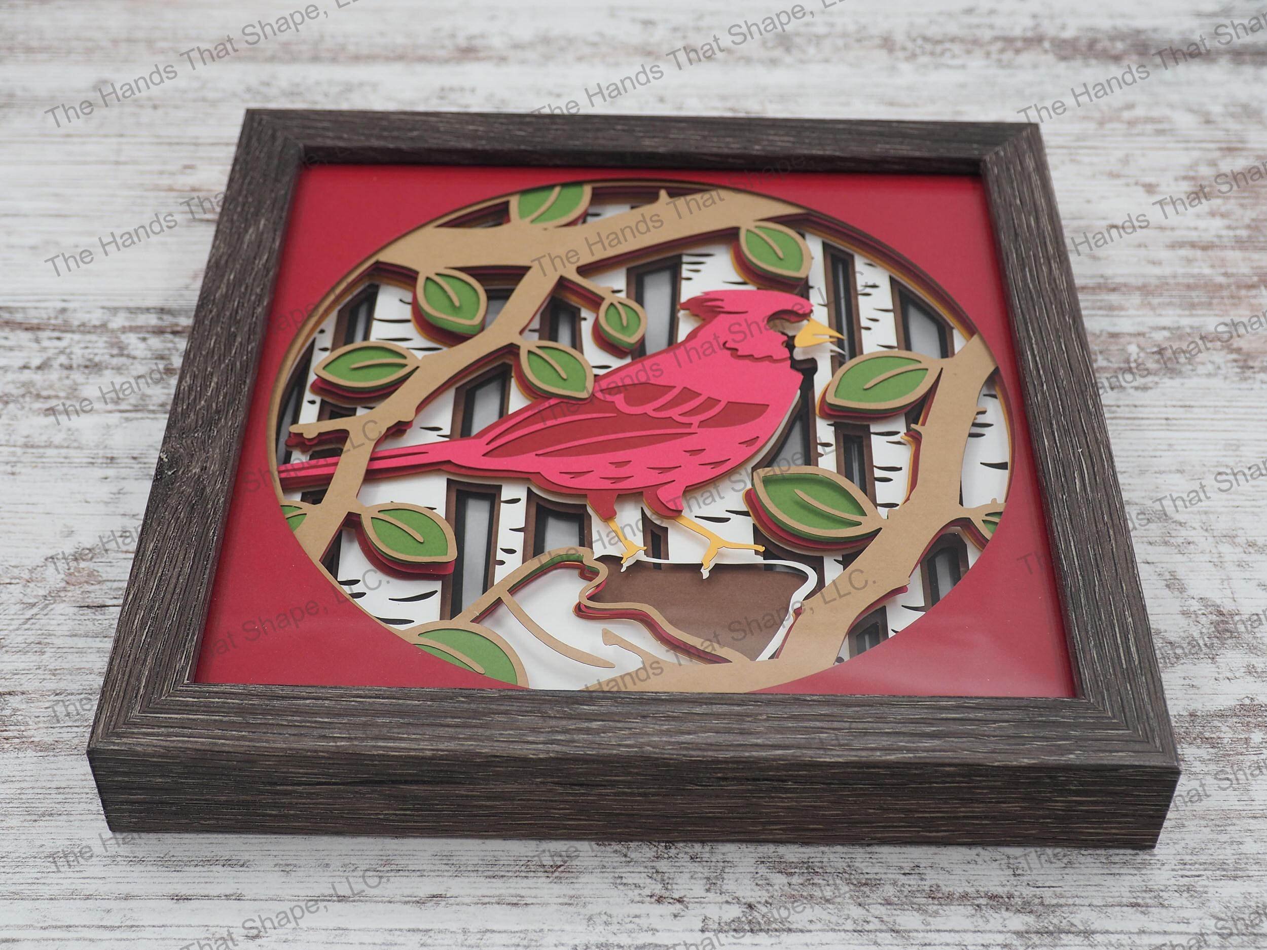 The shadow box features layers of cardstock paper to create a 3d picture of a cardinal perched against a birch forest background.