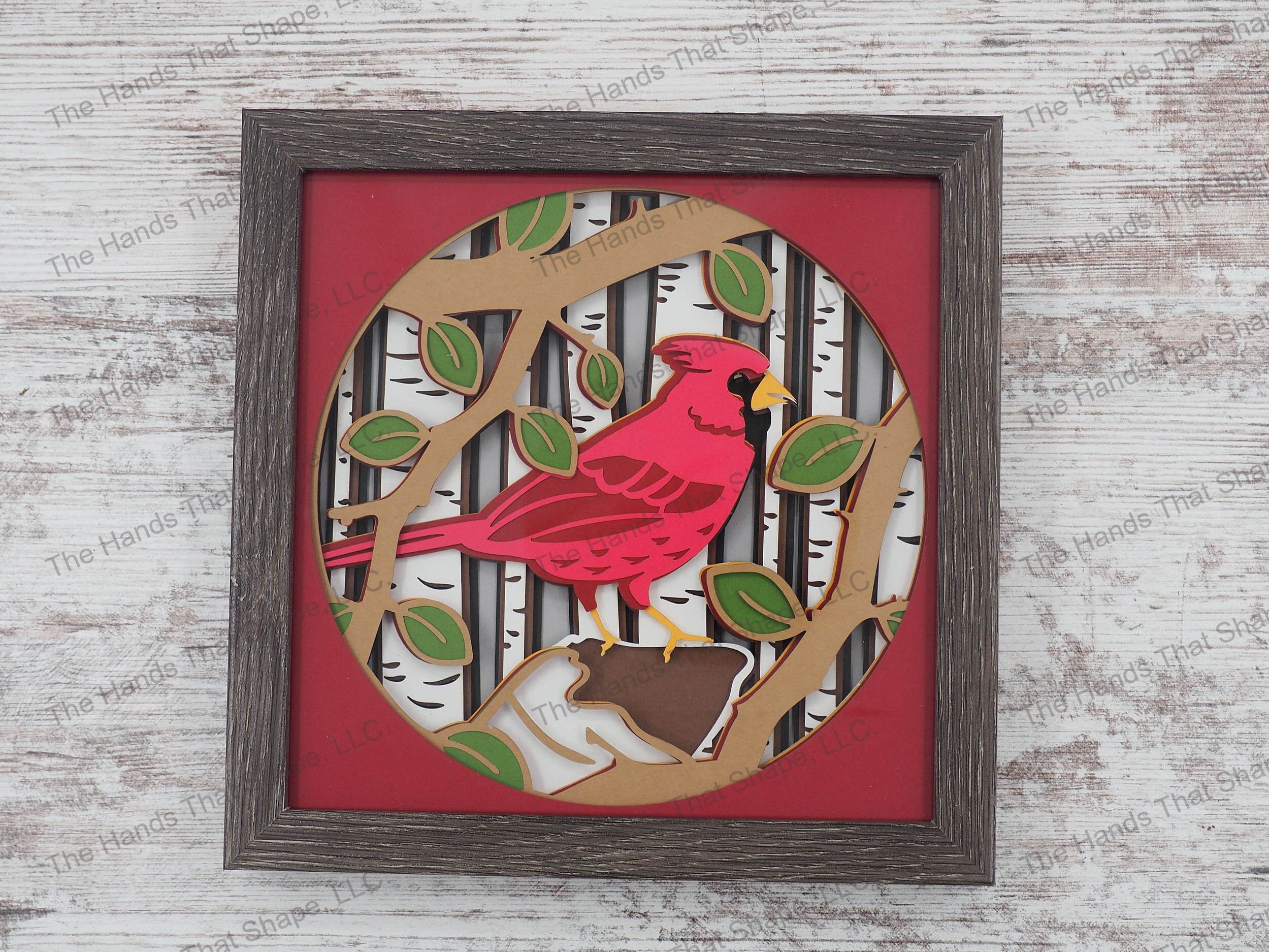The shadow box features layers of cardstock paper to create a 3d picture of a cardinal perched against a birch forest background.