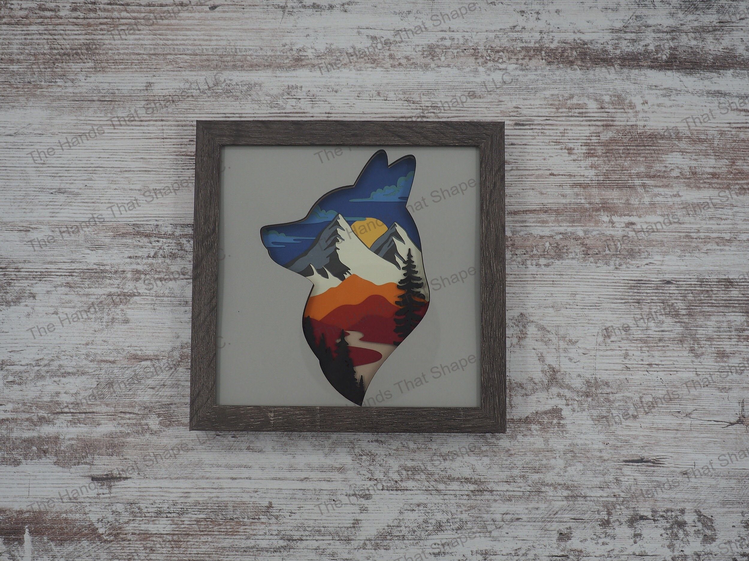 The shadow box features layers of cardstock paper to create a 3d picture of a towering mountain range, a river valley along with a pine forest within a fox head silhouette.