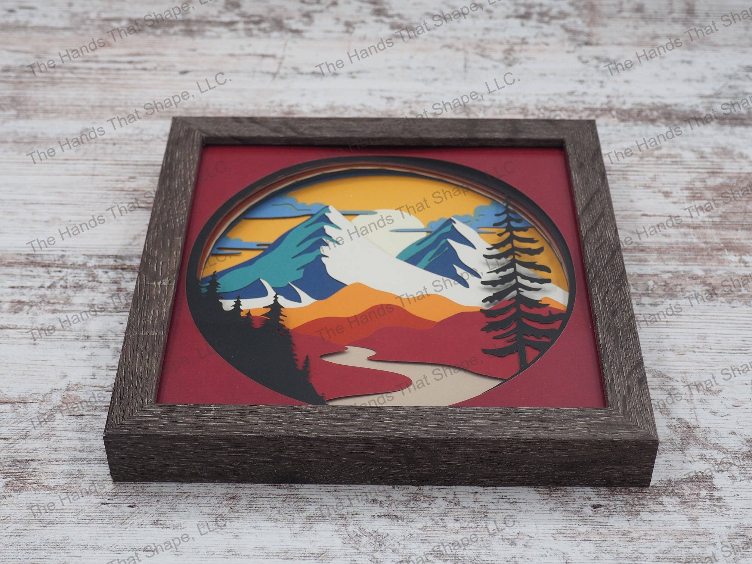 The “Red Mountain” shadowbox features mountains towering over rolling hills and a river. This shadowbox variation contains reds, oranges, blues and teals.