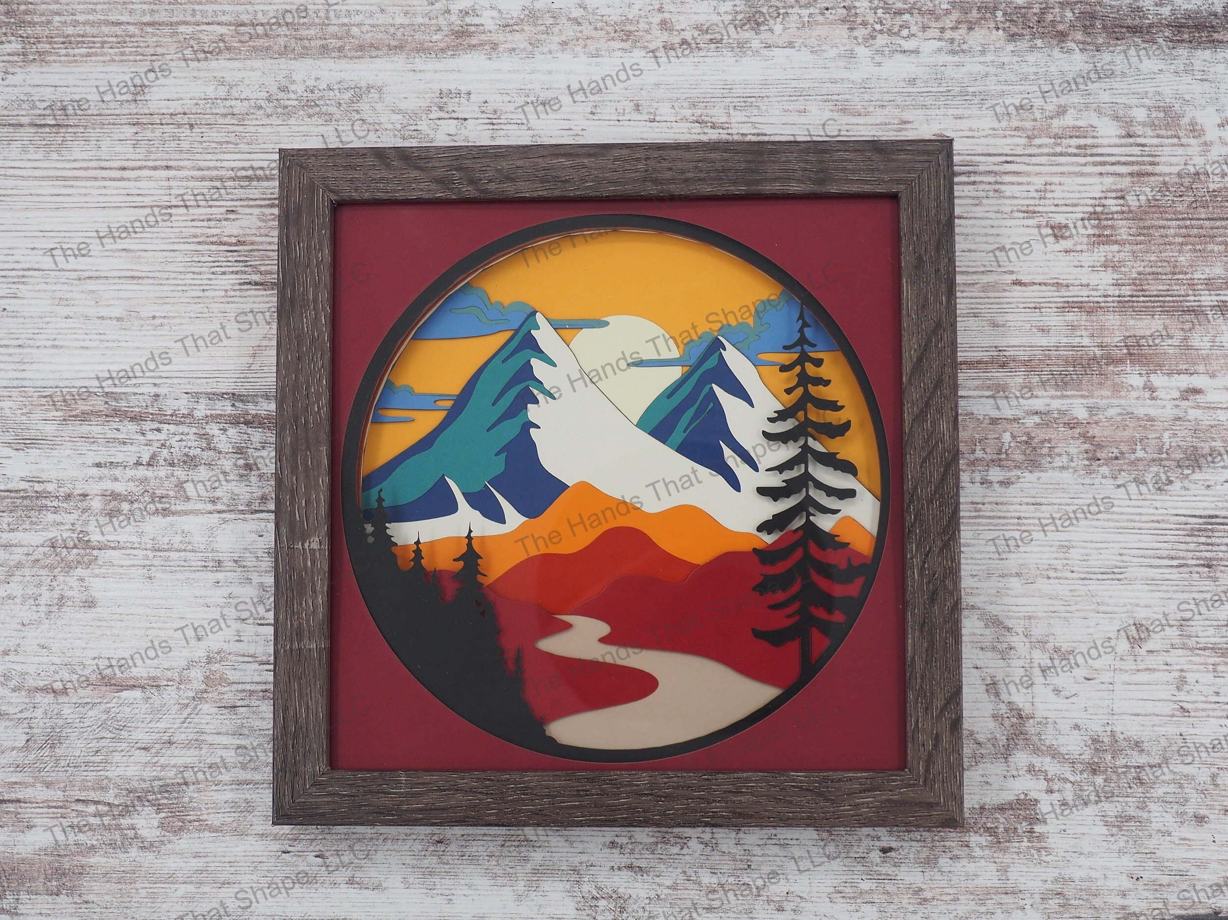 The “Red Mountain” shadowbox features mountains towering over rolling hills and a river. This shadowbox variation contains reds, oranges, blues and teals.