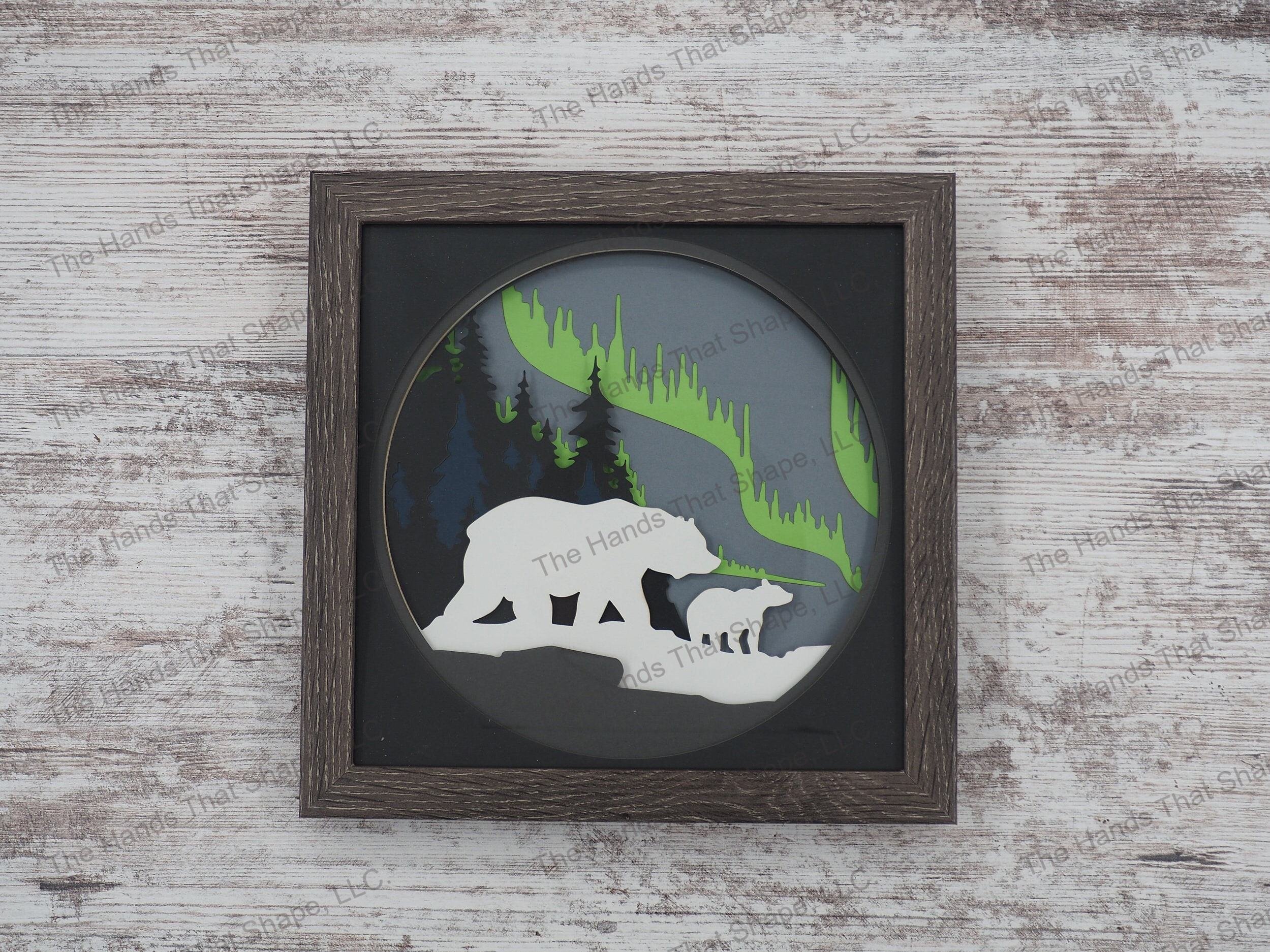 The shadow box features layers of cardstock paper to create a 3d picture of a mama bear and cub gazing at the mesmerizing northern lights.