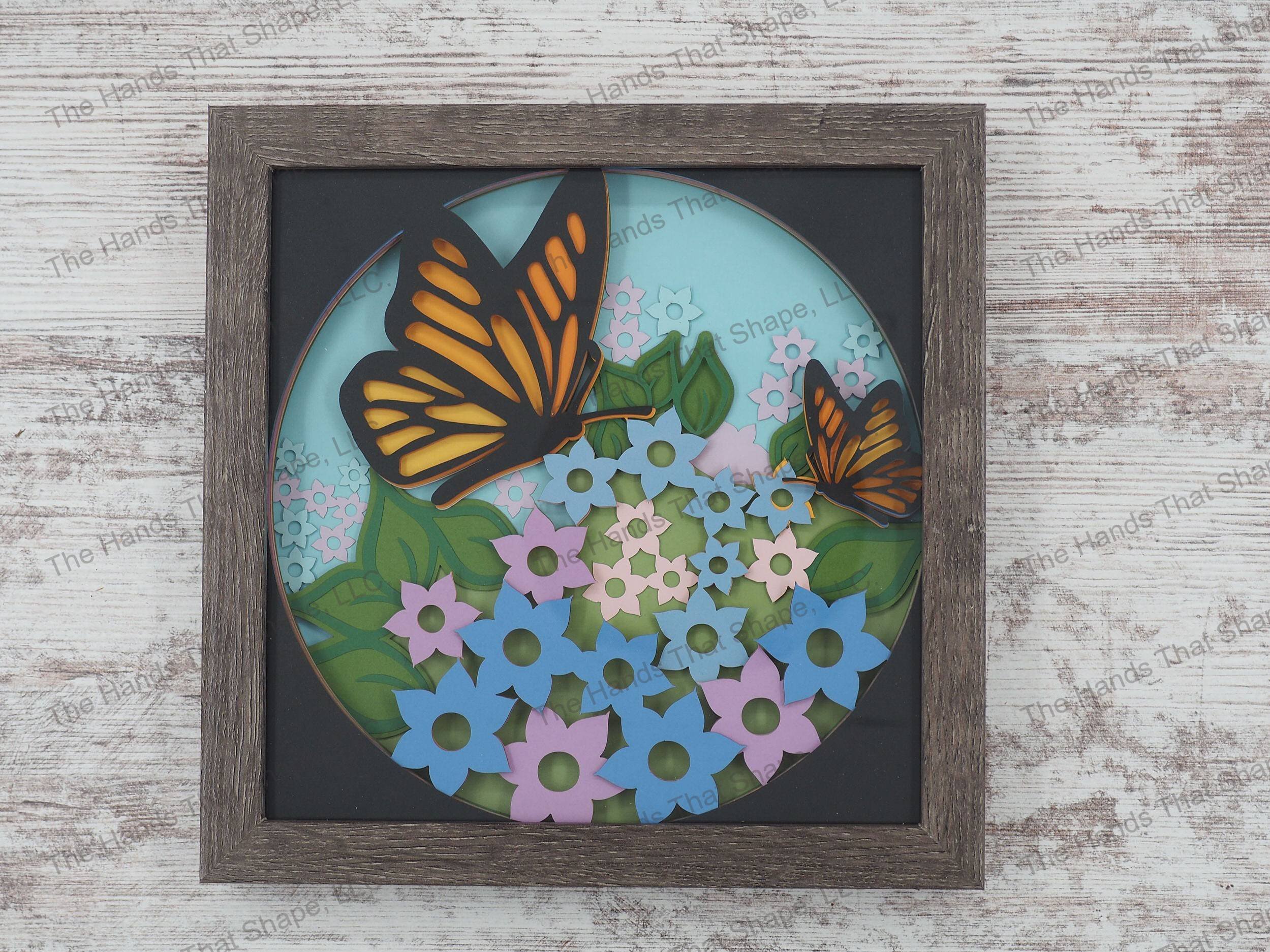 The shadow box features layers of cardstock paper to create a 3d picture of monarch butterflies stopping to rest among a field of flowers.