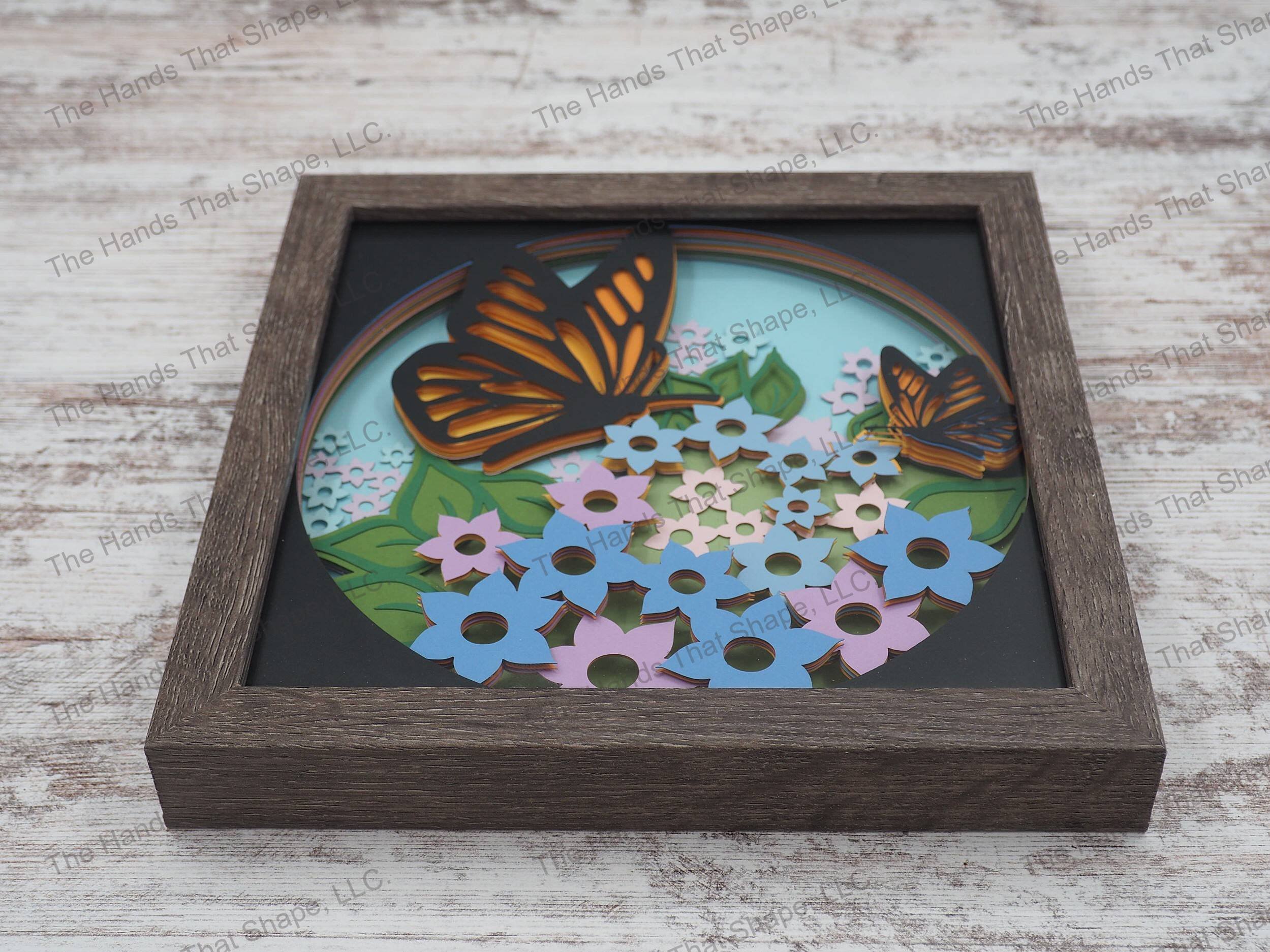 The shadow box features layers of cardstock paper to create a 3d picture of monarch butterflies stopping to rest among a field of flowers.