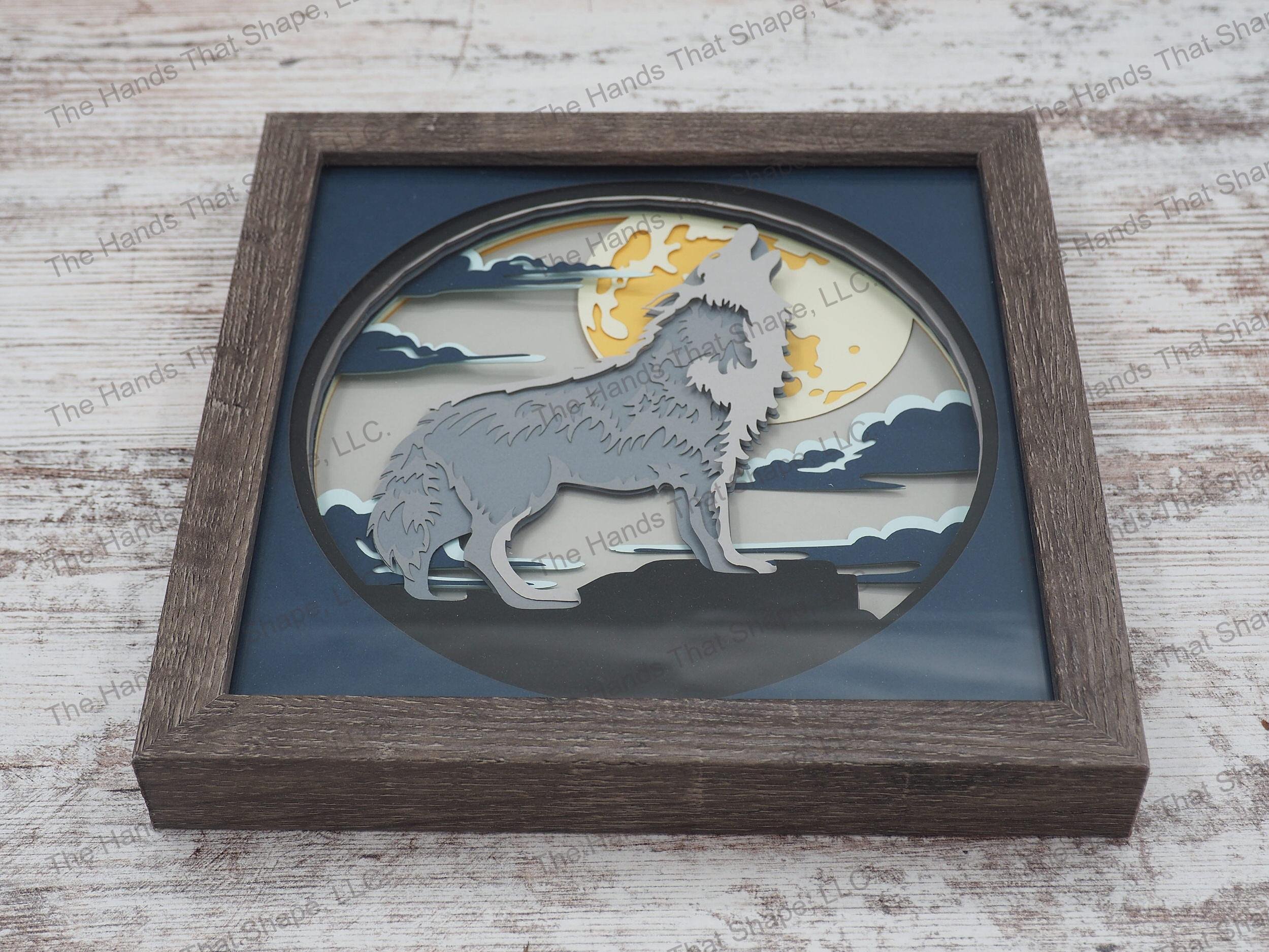 The “Howling Wolf” shadowbox features layers of cardstock paper to create a 3d picture of a lone wolf howling against the background of a full moon.