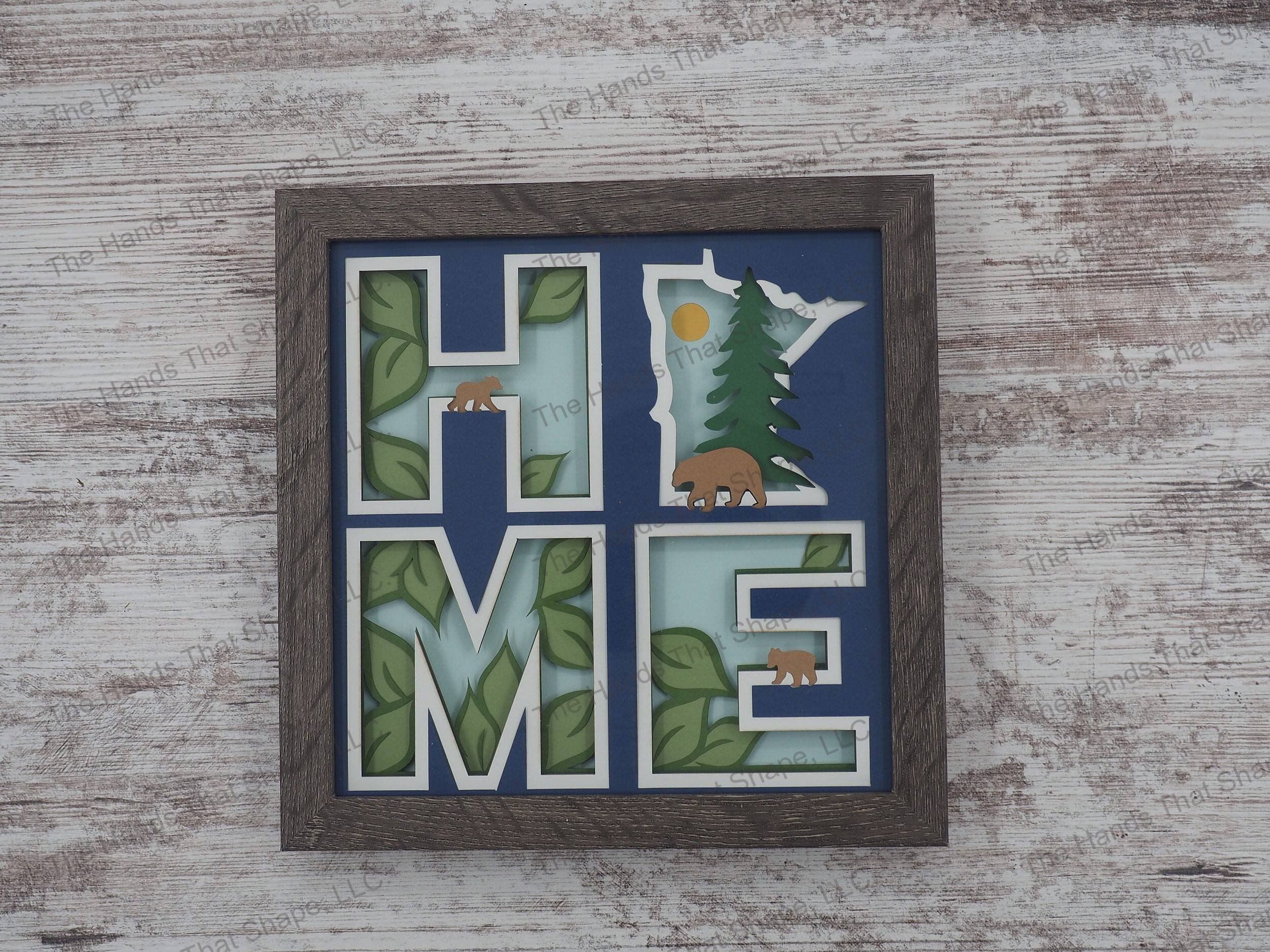 The shadow box spells out “Home” utilizing the state of Minnesota as the “O” and features a mama bear and cubs against a forest/nature backdrop.