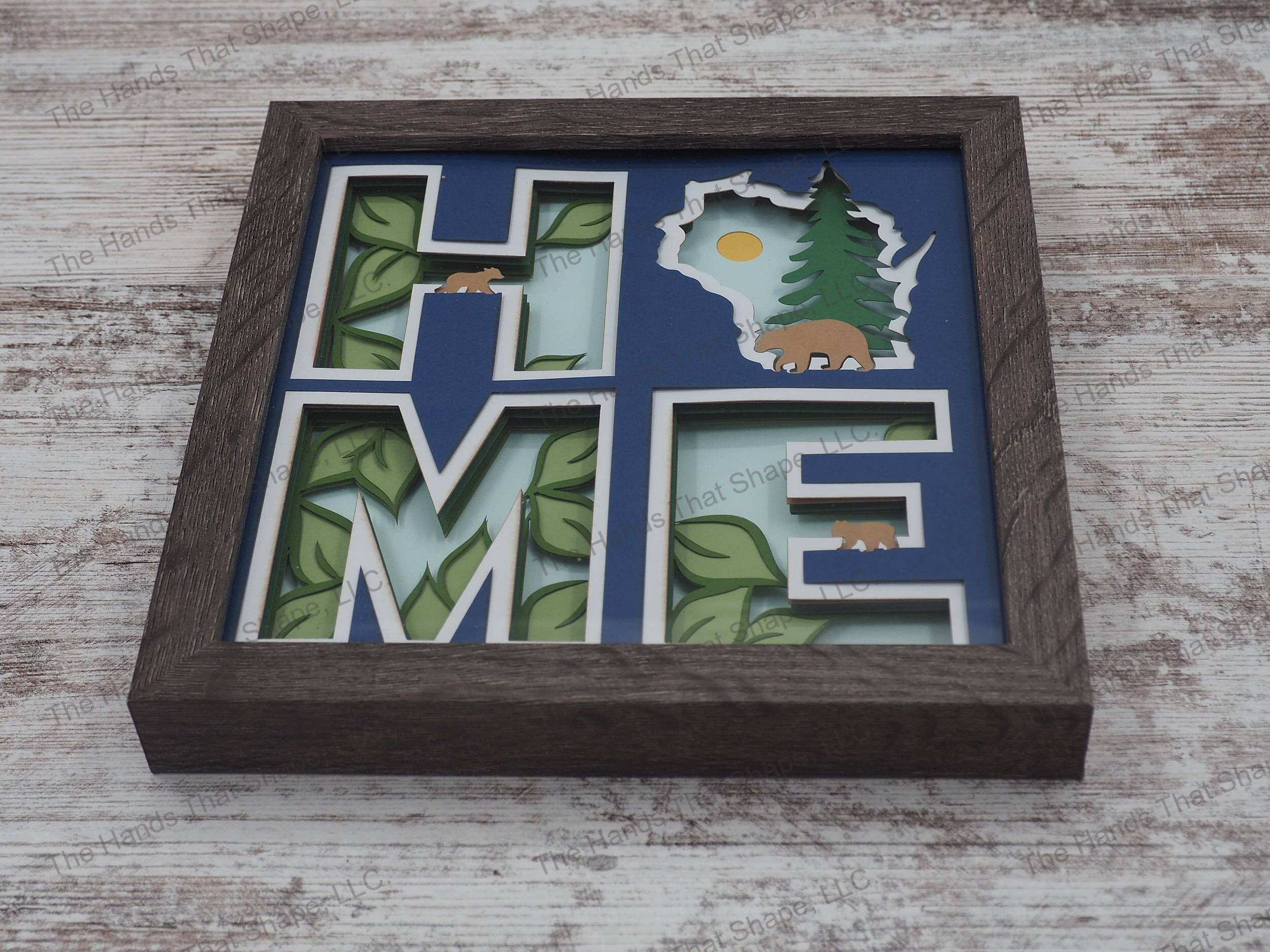 The shadow box spells out “Home” utilizing the state of Wisconsin as the “O” and features a mama bear and cubs against a forest/nature backdrop.