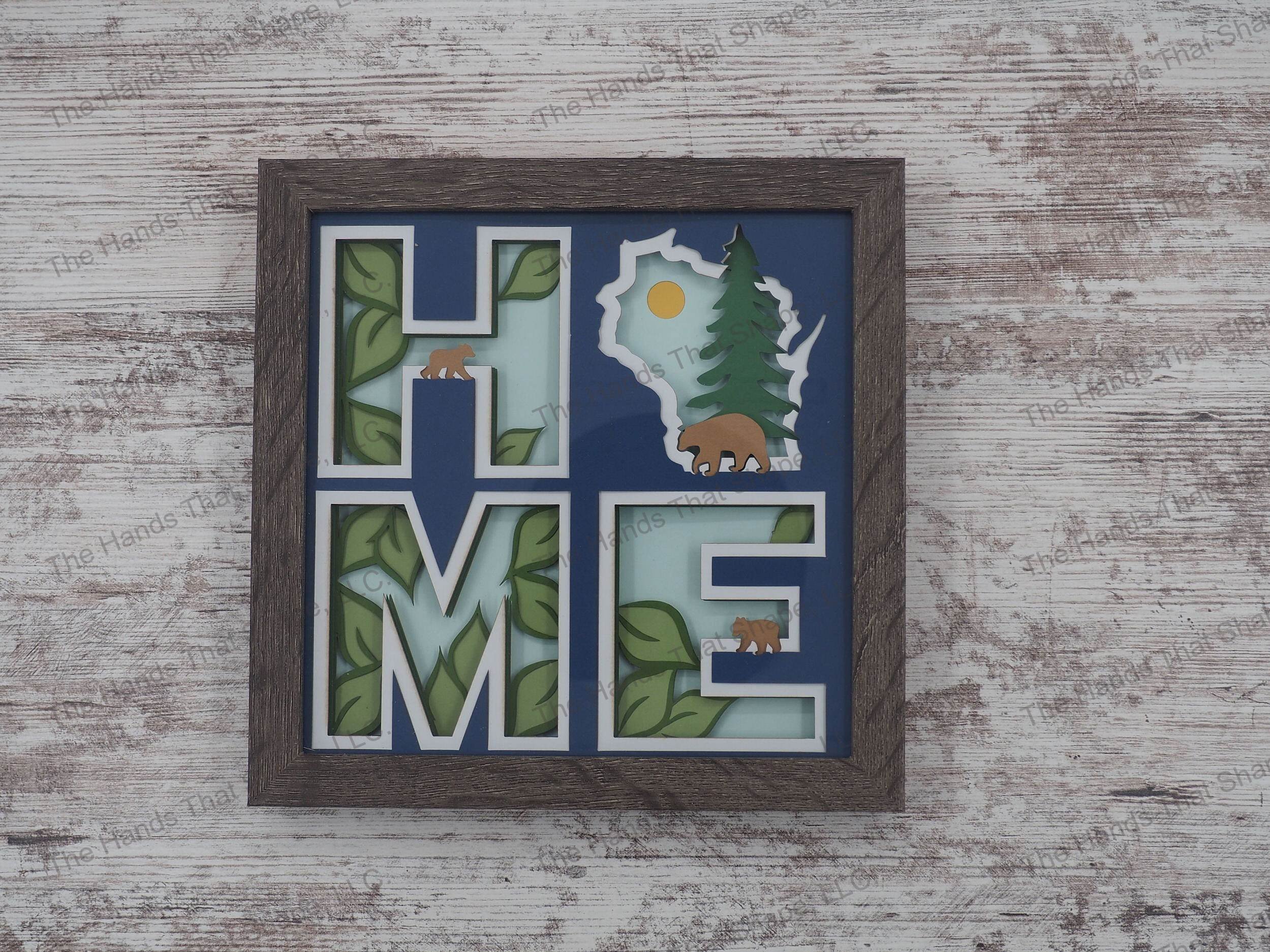 The shadow box spells out “Home” utilizing the state of Wisconsin as the “O” and features a mama bear and cubs against a forest/nature backdrop.