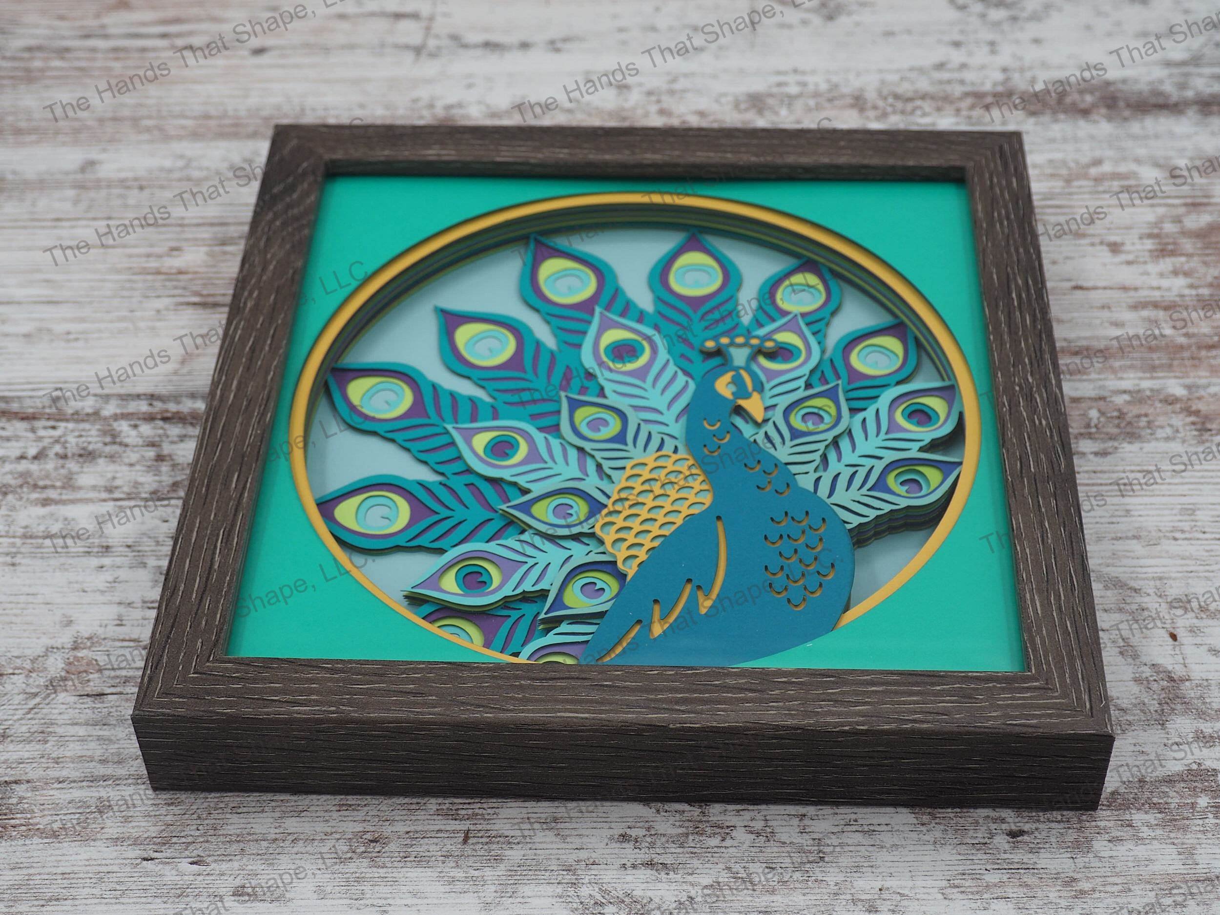 The “Peacock” shadowbox features layers of cardstock paper to create a 3d picture of a peacock, and it's magnificent feathers on full display.