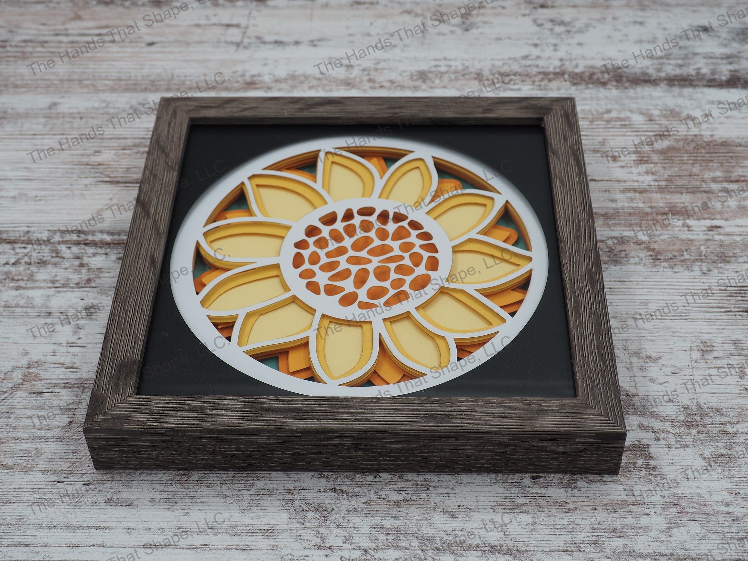 The shadow box features layers of cardstock paper to create a 3d picture of a large vibrant yellow sunflower.