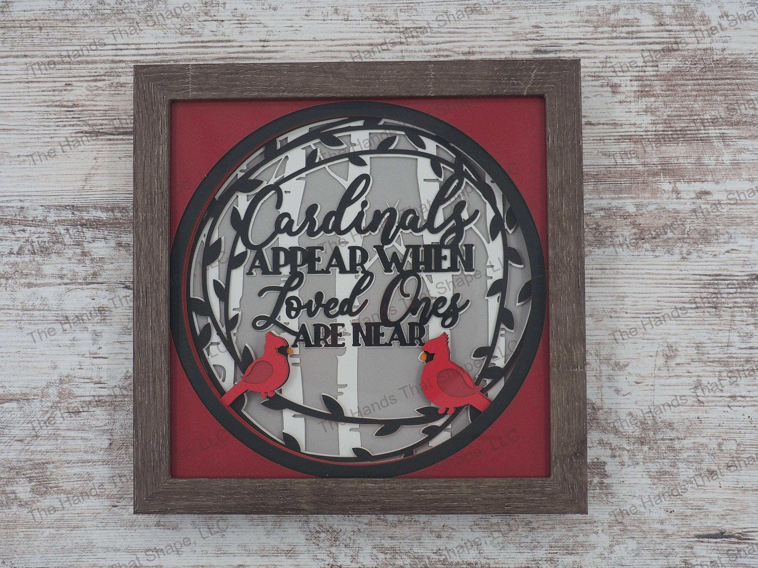 The shadow box features the phrase “Cardinals appear when loved ones are near” and features two red cardinals sitting on a black leaf wreath in a birch forest.