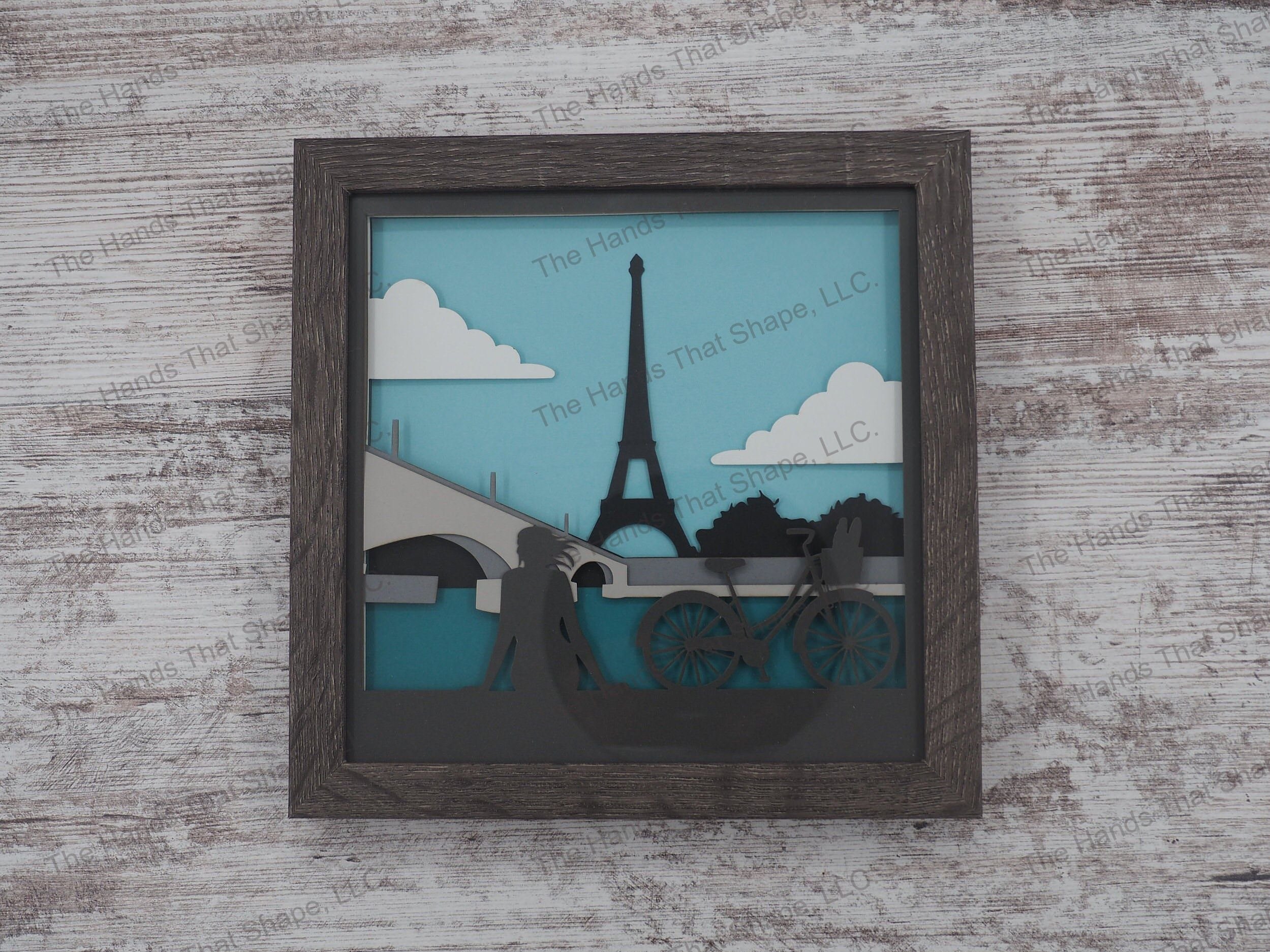 The “Paris” shadowbox features a bicyclist resting along the Seine and overlooking the beautiful Eiffel Tower.