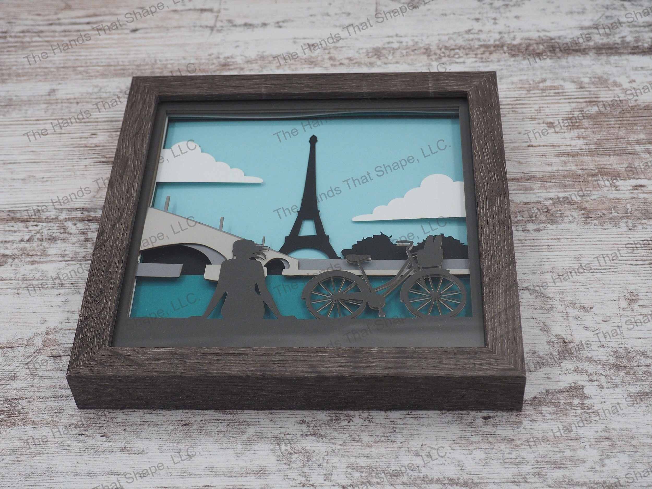 The “Paris” shadowbox features a bicyclist resting along the Seine and overlooking the beautiful Eiffel Tower.