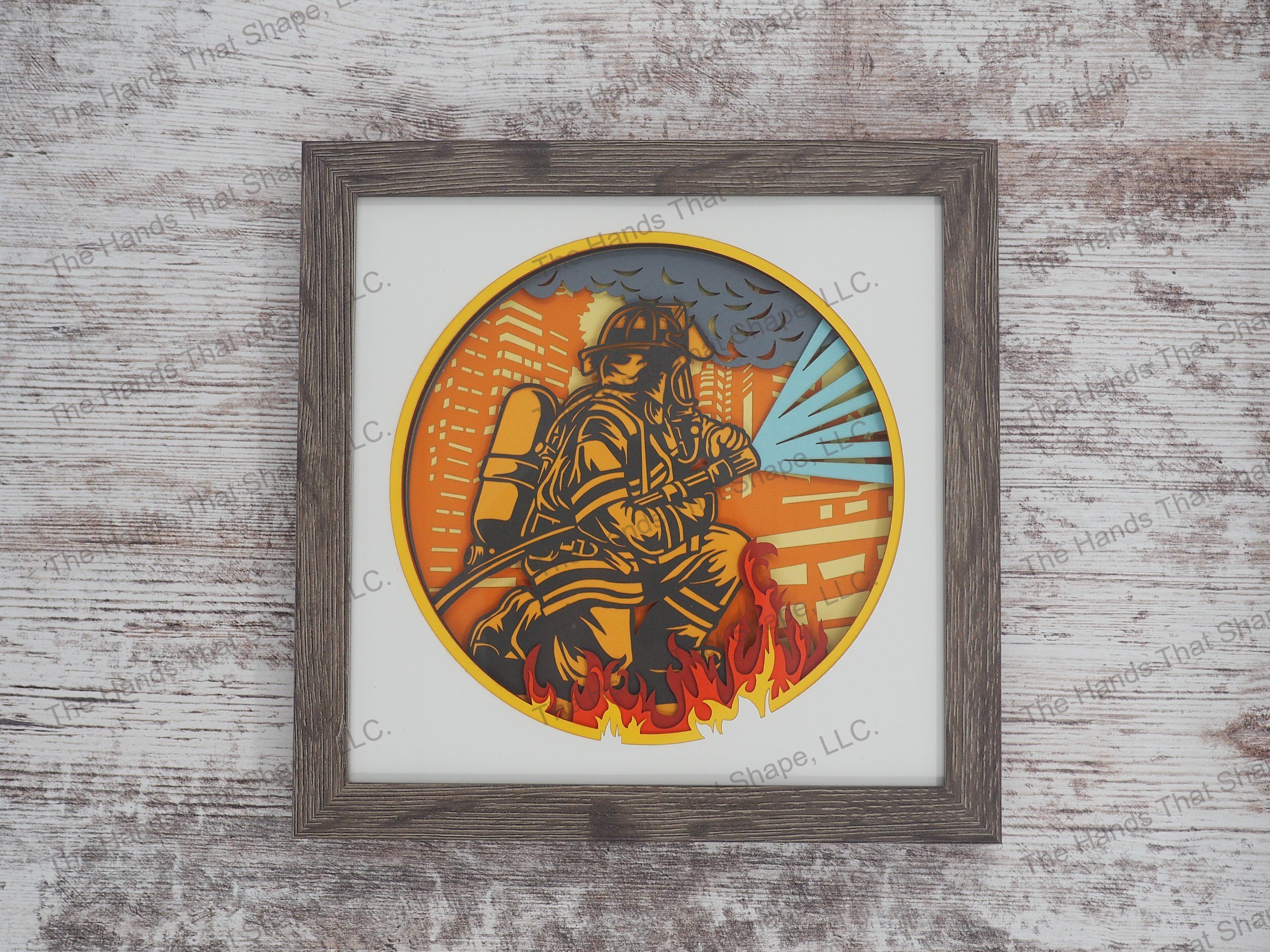 The shadow box features layers of cardstock paper to create a 3d picture of a firefighter in full gear working to extinguish a large building fire.