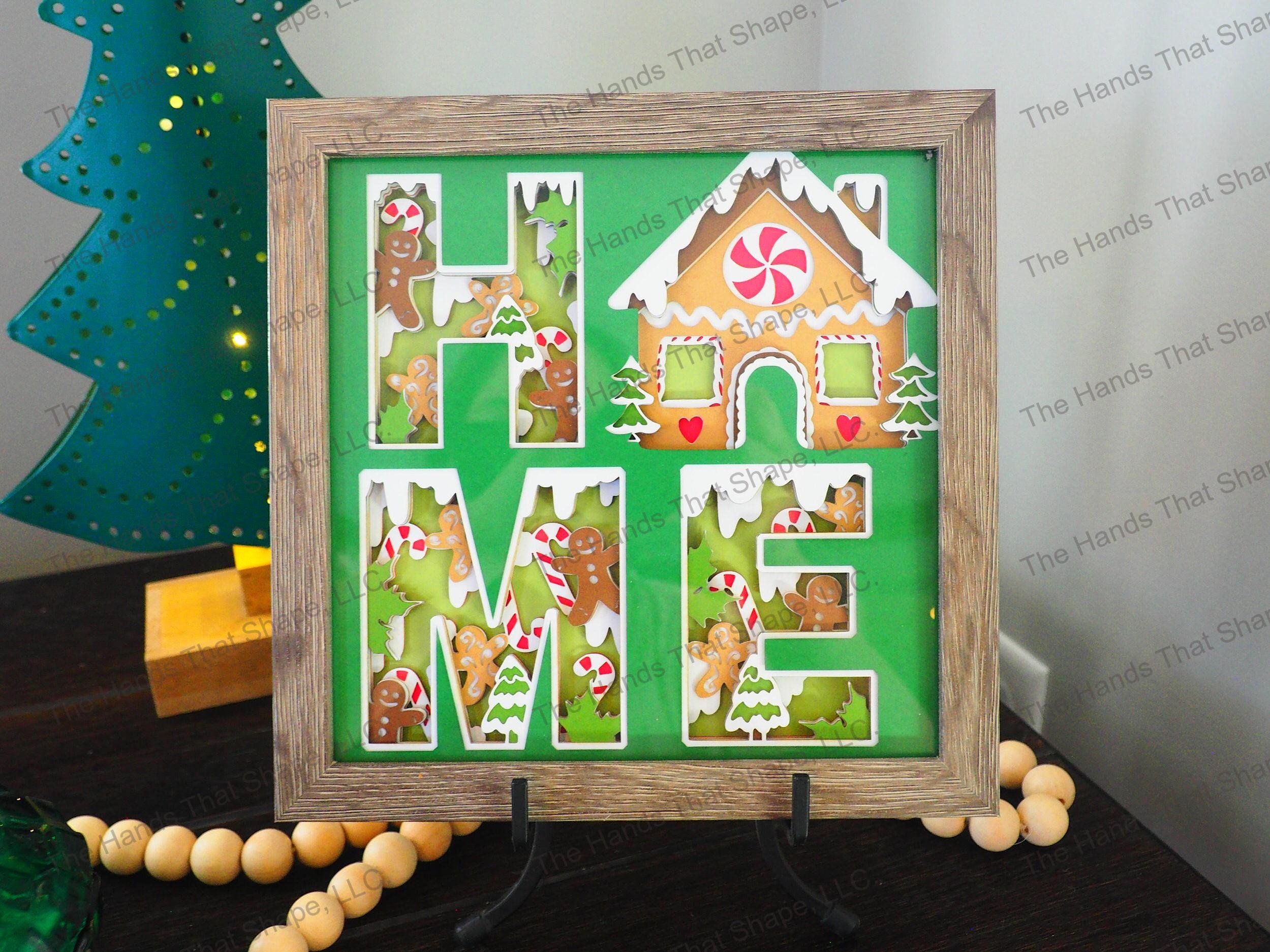 The shadow box features the word "HOME" cutout and filled-in with holiday themed cookies and candy canes. The "O" was replaced with a very festive Gingerbread House.