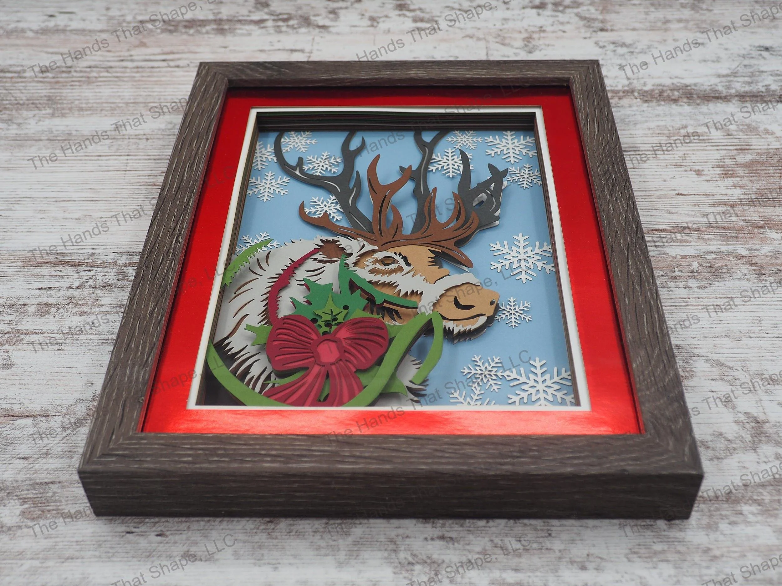 The “Reindeer” layered paper / cardstock shadow box features a lone reindeer adored with a Christmas bow.
