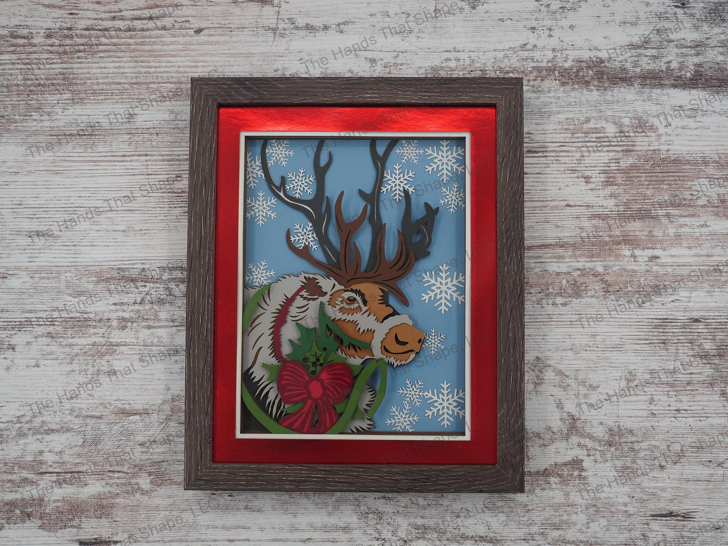 The “Reindeer” layered paper / cardstock shadow box features a lone reindeer adored with a Christmas bow.