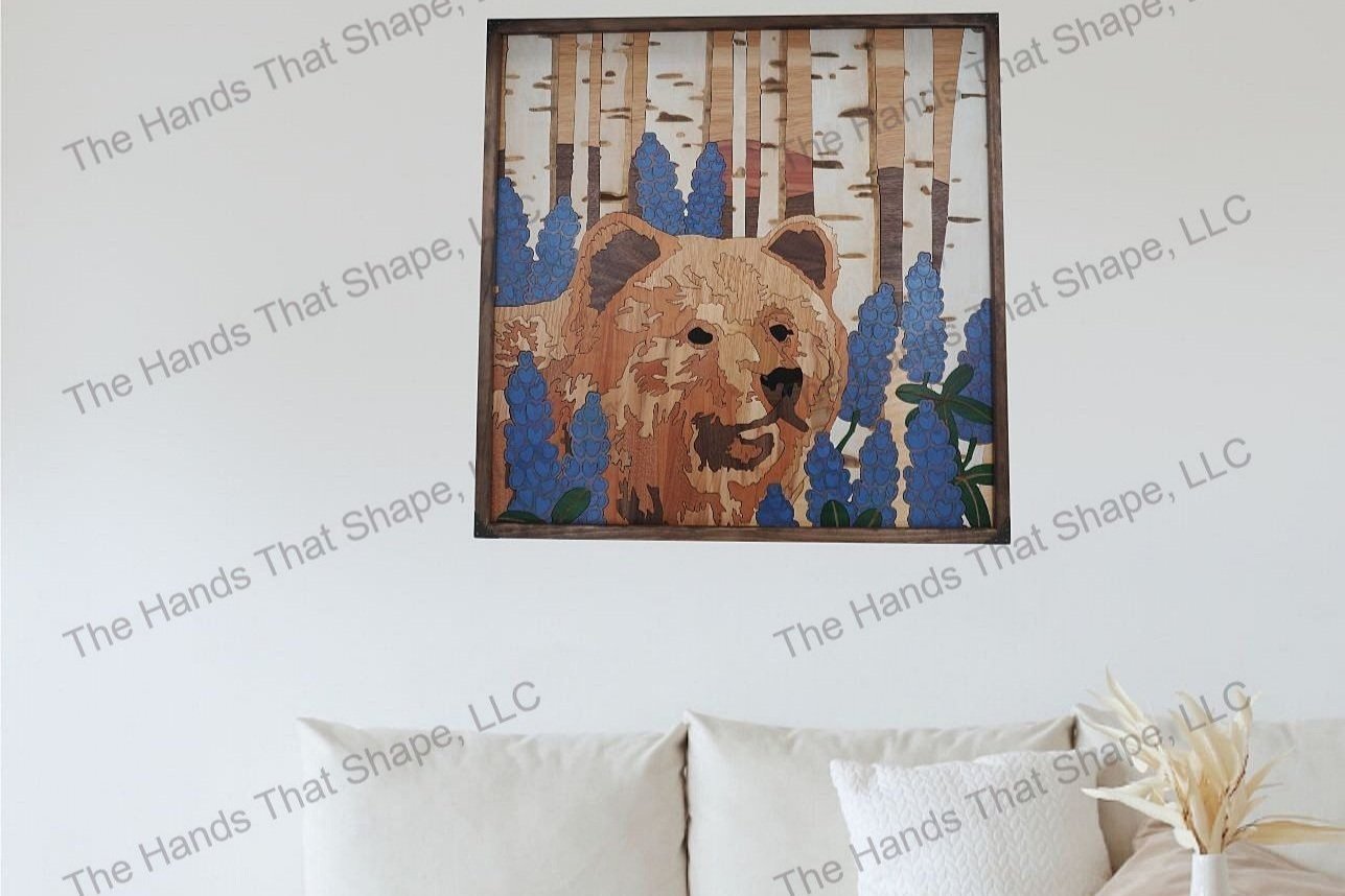 Finished bear and lupines wood wall art piece staged on a living room wall above a sofa or couch and coffee table.