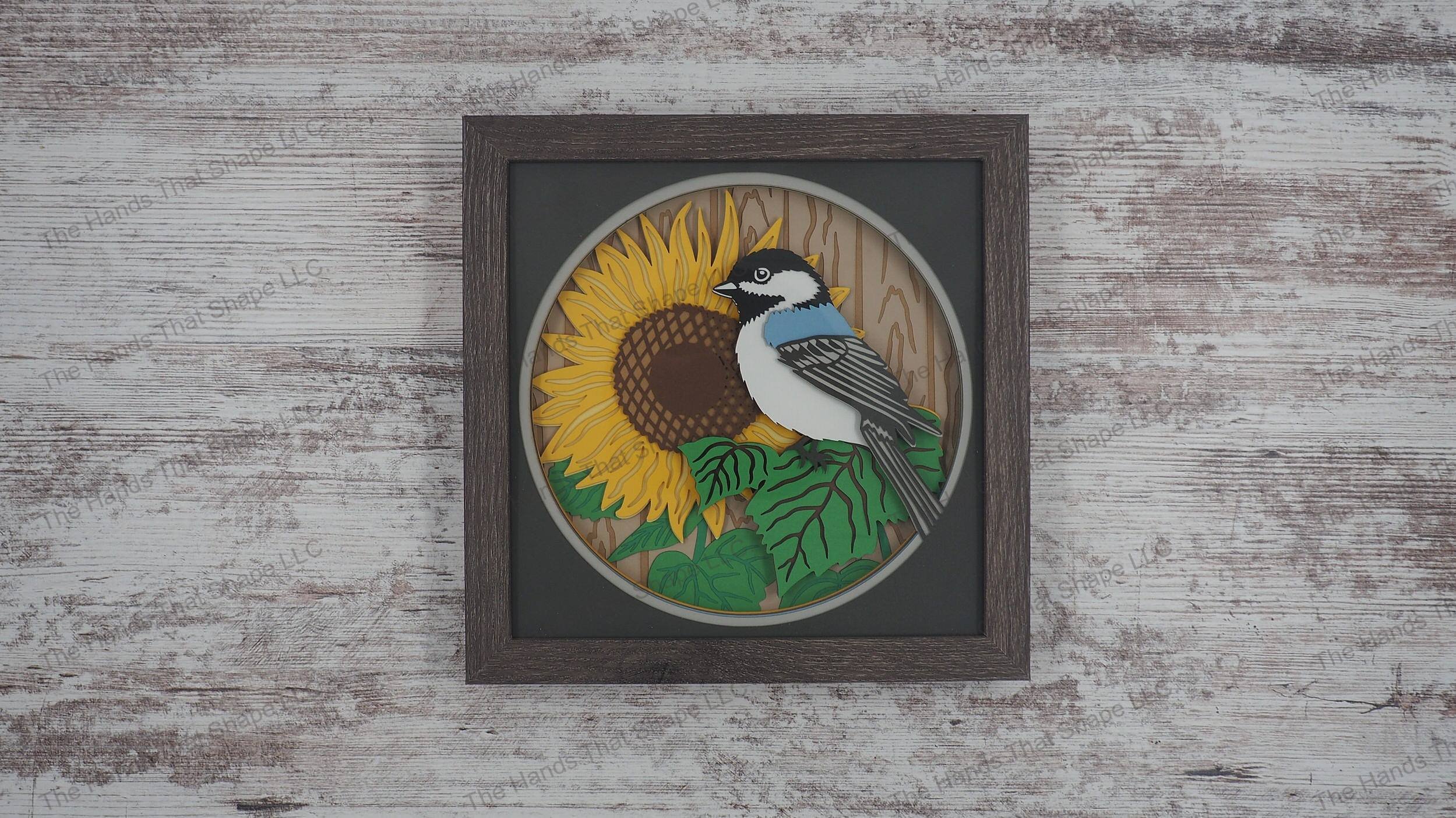 3D shadowbox with a chickadee on sunflower leaves, a large bloom, and a slat fence background, crafted from 15 layers of premium cardstock.