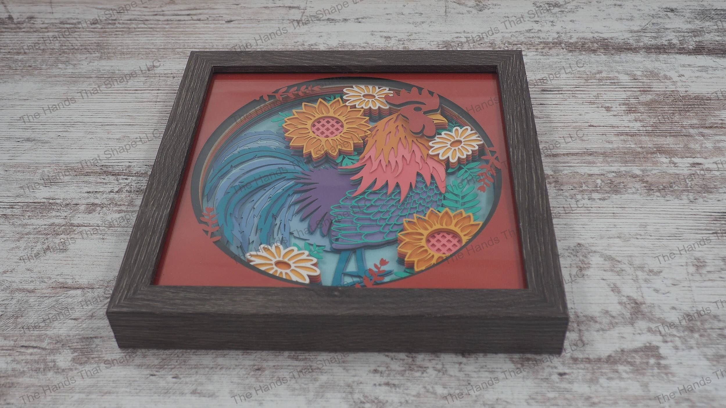 Vibrant 'Boho Chicken' shadowbox with colorful feathers and flowers in 14-layer cardstock, framed in glass-covered gray MDF for a 3D effect.