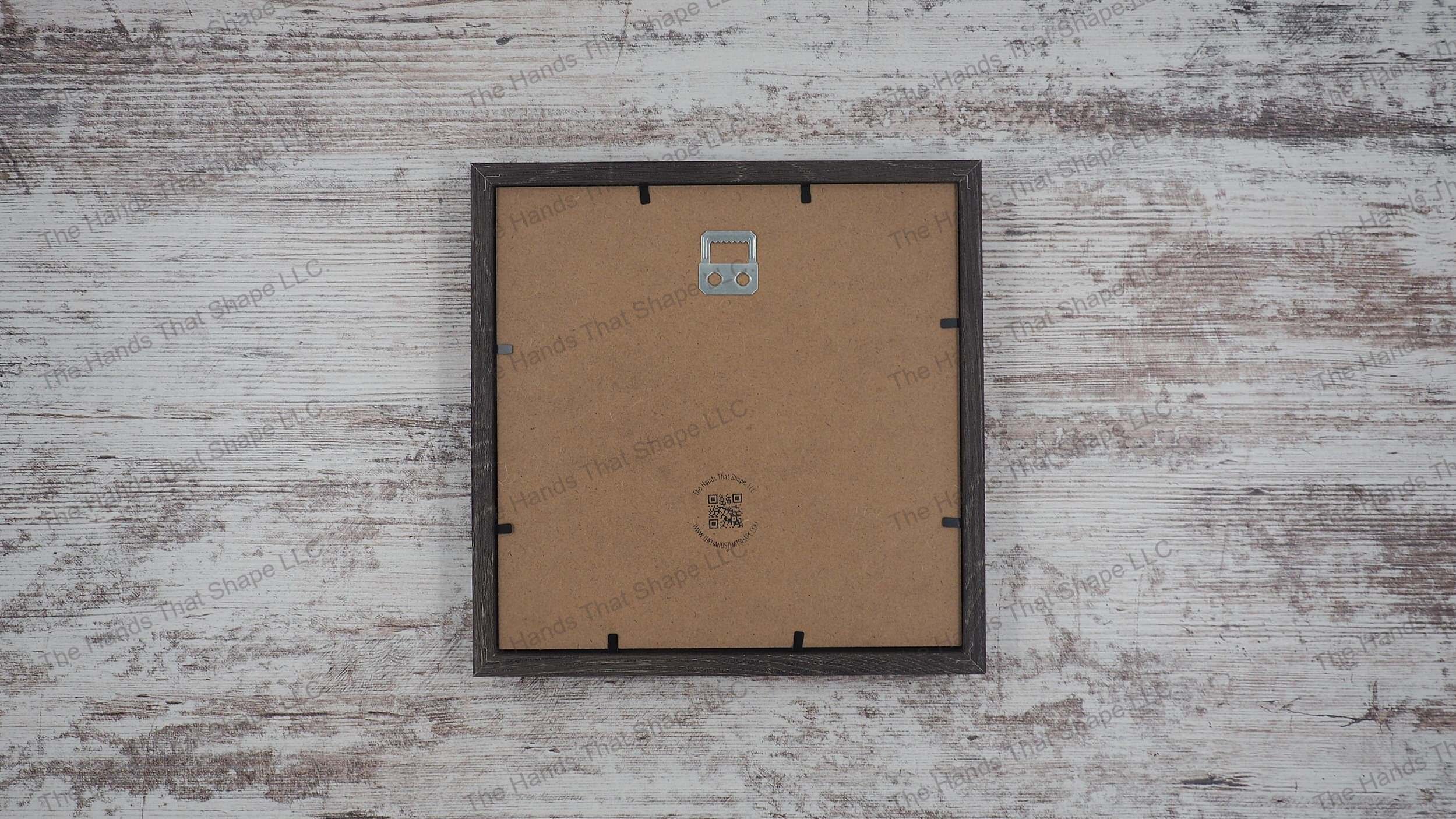 The back side of the layered cardstock paper shadow box that uses sheets of paper to create a 3d image. The backside shows The Hands That Shape, LLC logo and mounted hanger.
