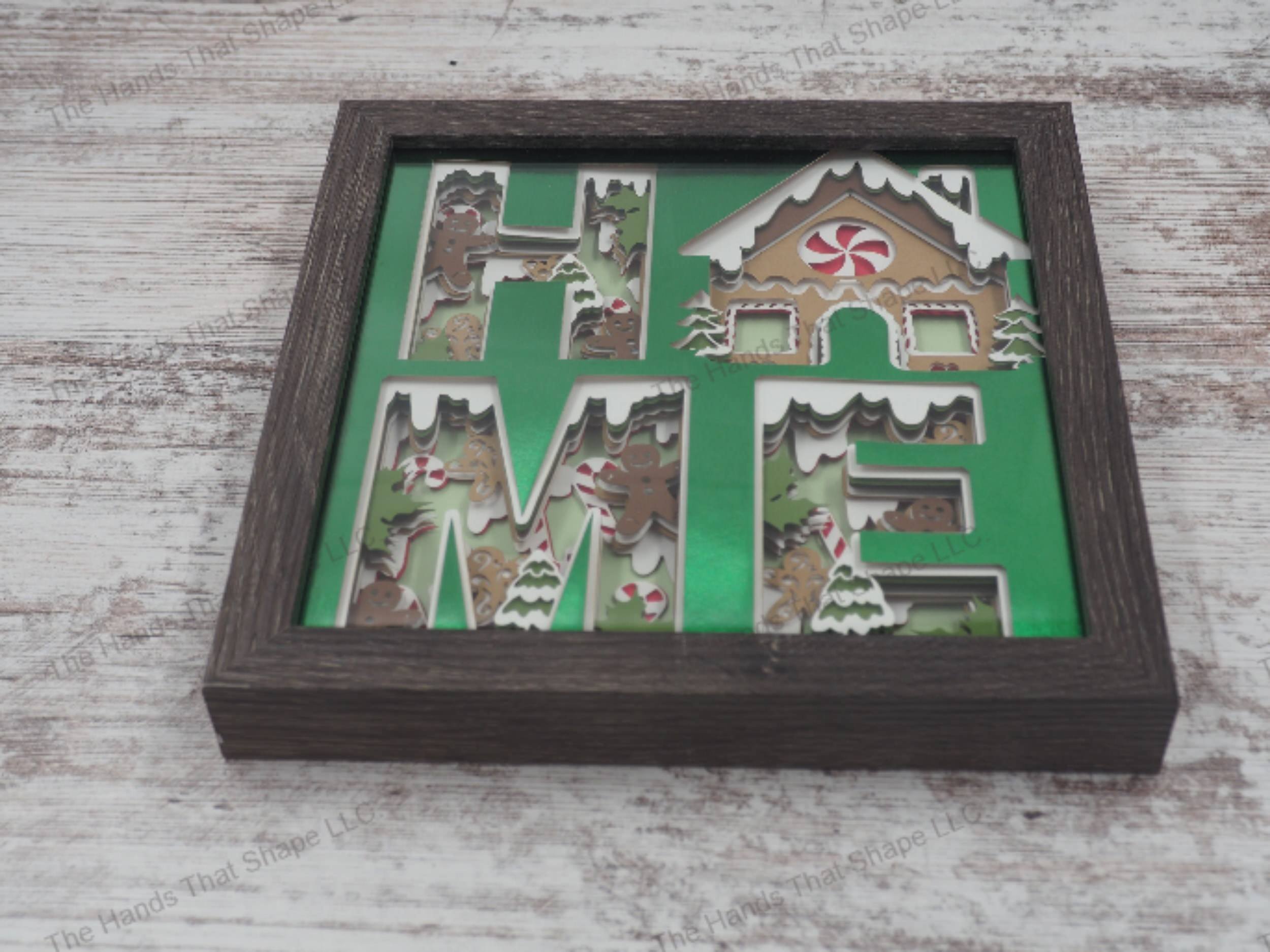 The shadow box features the word "HOME" cutout and filled-in with holiday themed cookies and candy canes. The "O" was replaced with a very festive Gingerbread House.