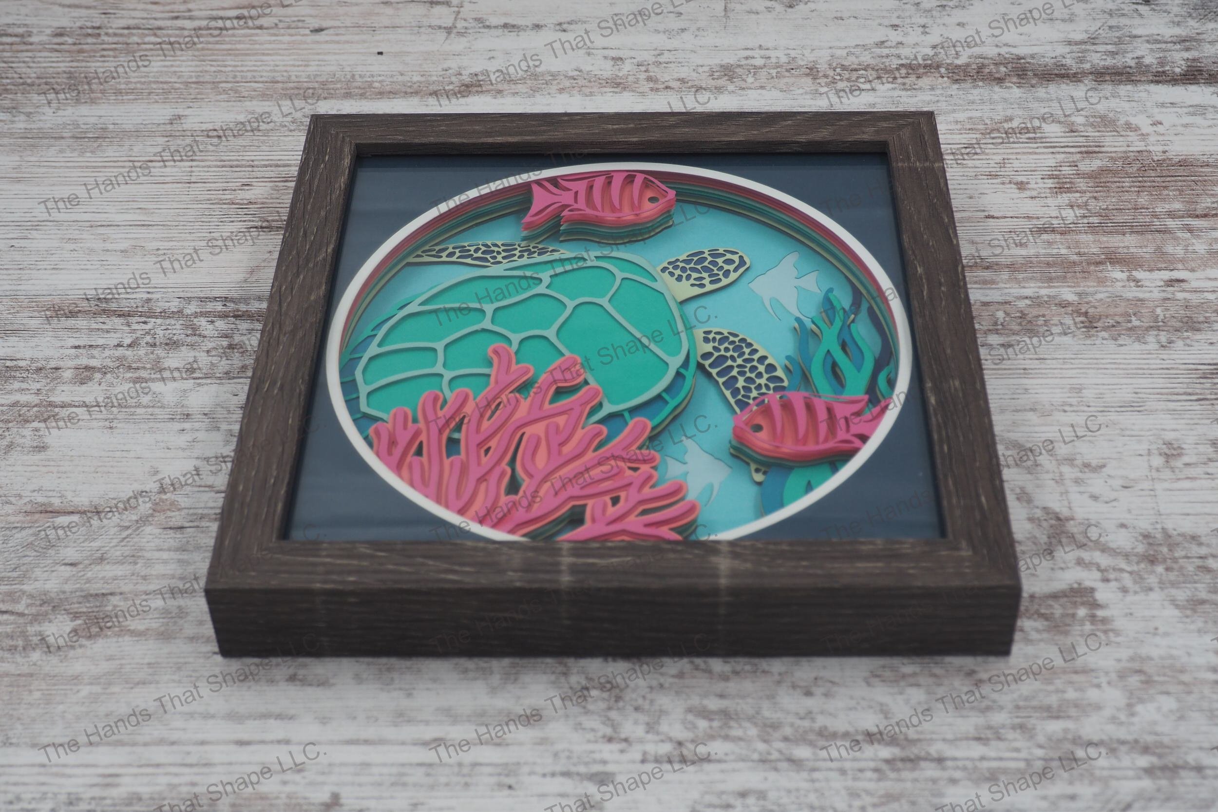 A layered paper shadowbox depicting an underwater scene with a sea turtle, tropical fish, and coral, crafted from 12 layers of cardstock in a gray MDF frame.