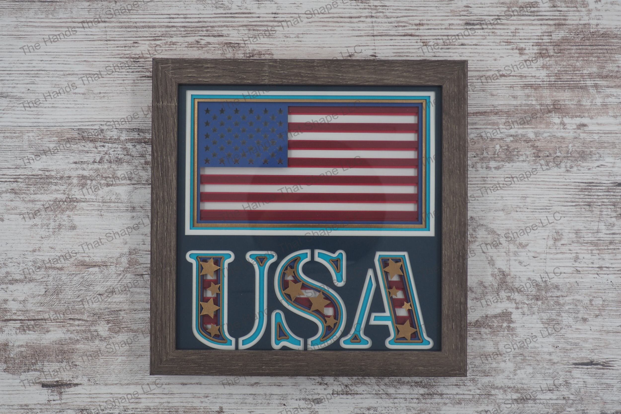A layered paper shadowbox showcasing the American flag and 'USA' with gold foil stars and striped background, 8 layers of cardstock in a gray MDF frame.