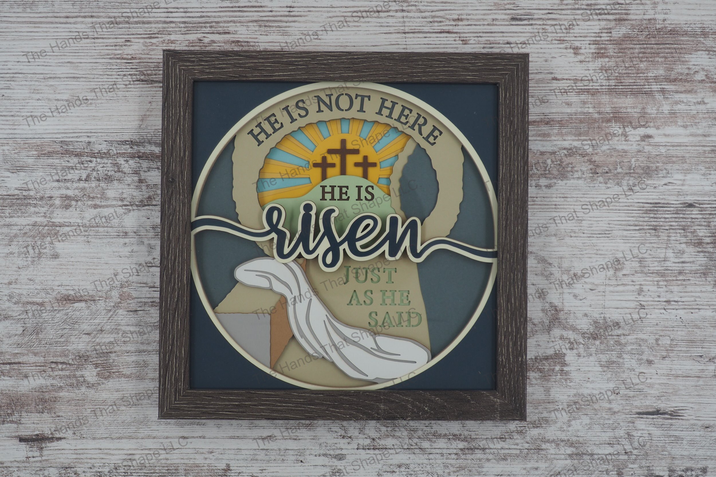 A layered paper shadowbox depicting the resurrection scene with 'risen' text, crafted from 13 layers of cardstock in a gray MDF frame.