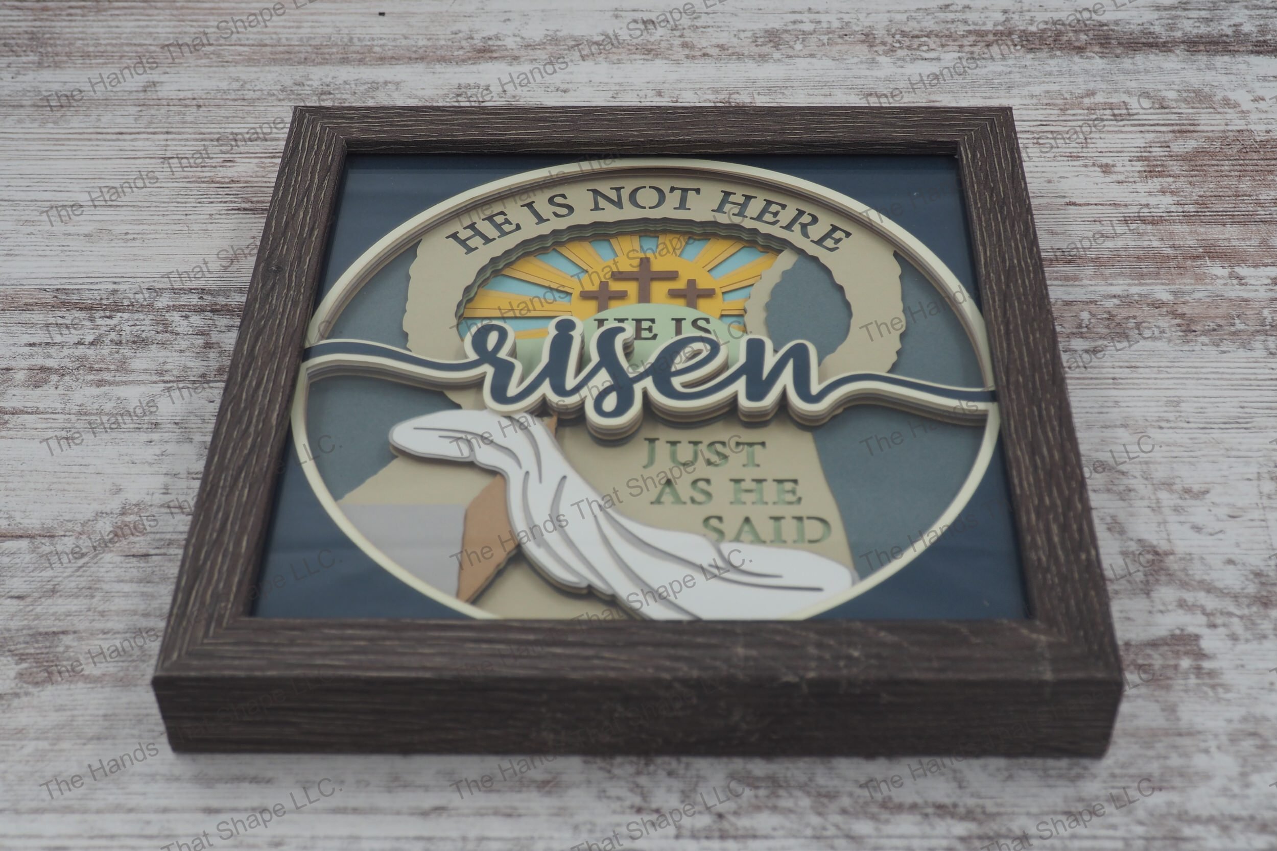 A layered paper shadowbox depicting the resurrection scene with 'risen' text, crafted from 13 layers of cardstock in a gray MDF frame.