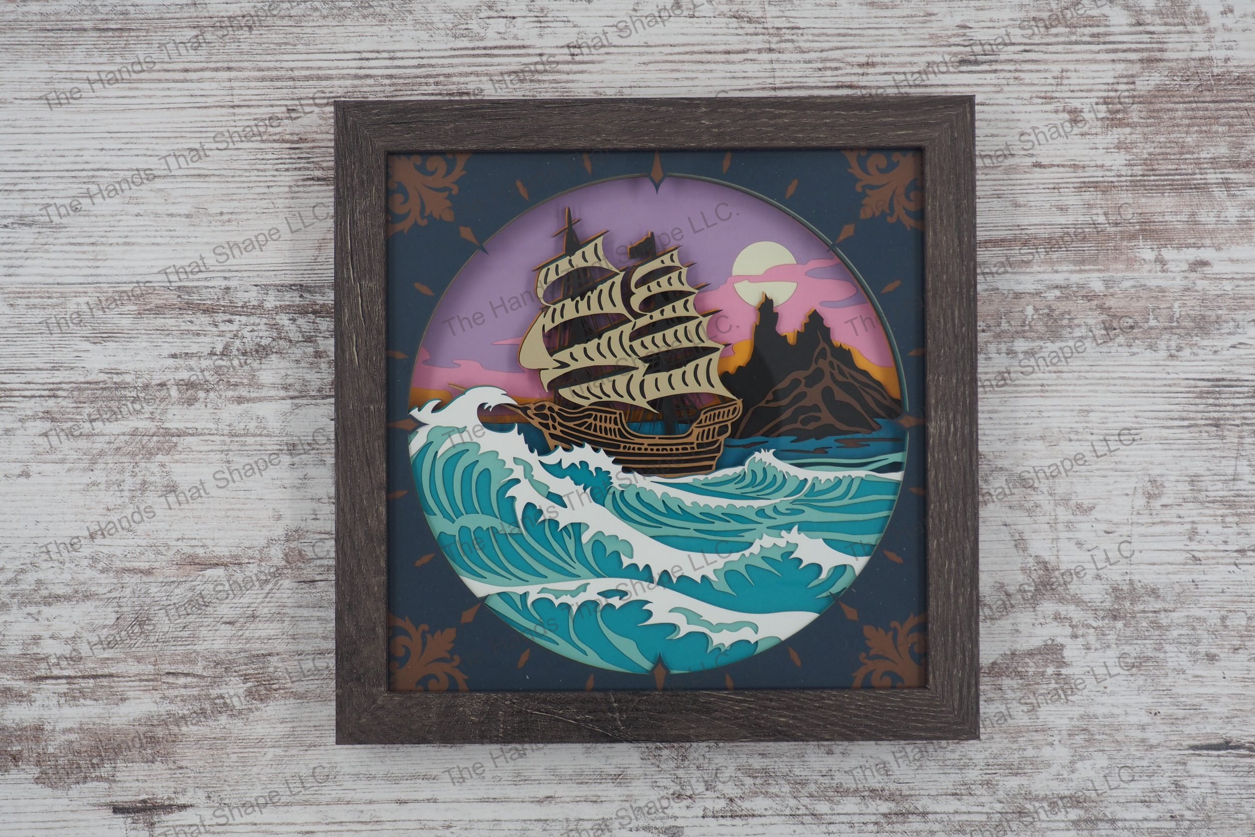 A detailed shadowbox featuring an old-world sailing ship navigating stormy seas made with 13 layers of cardstock, encased in a gray MDF frame with glass cover.