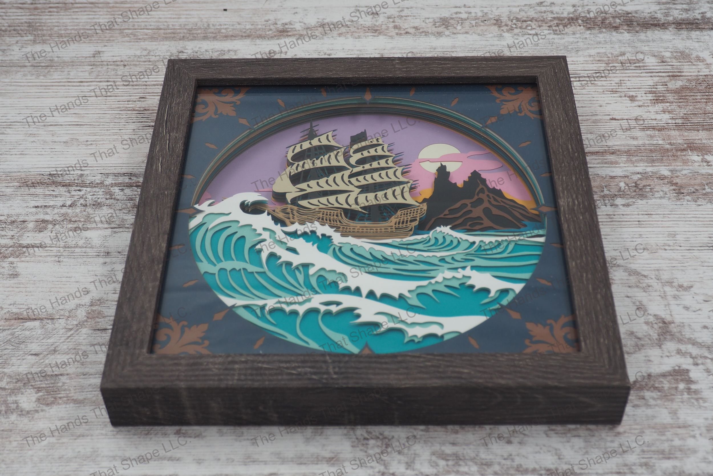 A detailed shadowbox featuring an old-world sailing ship navigating stormy seas made with 13 layers of cardstock, encased in a gray MDF frame with glass cover.