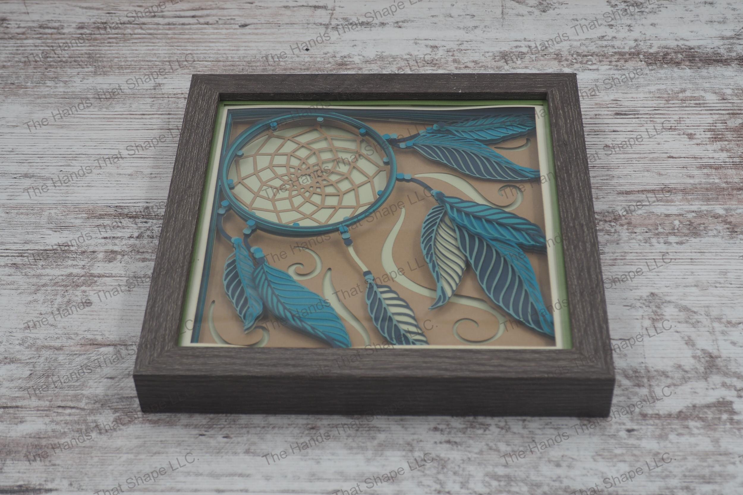 Dream Catcher layered paper shadowbox features a dream catcher, feather sets, and beaded cords on a swirled background, in 10-layer cardstock and gray frame.