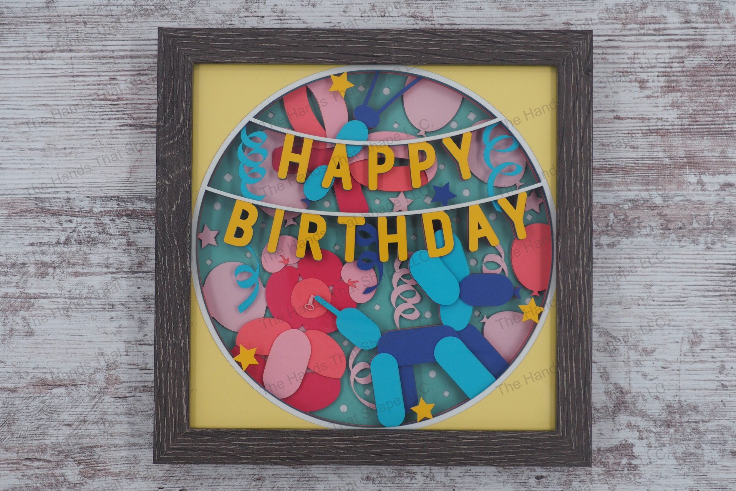 A celebratory shadowbox featuring 'Happy Birthday' banner, balloon animals, and party decorations in 13 layers of cardstock, encased in a gray MDF frame.