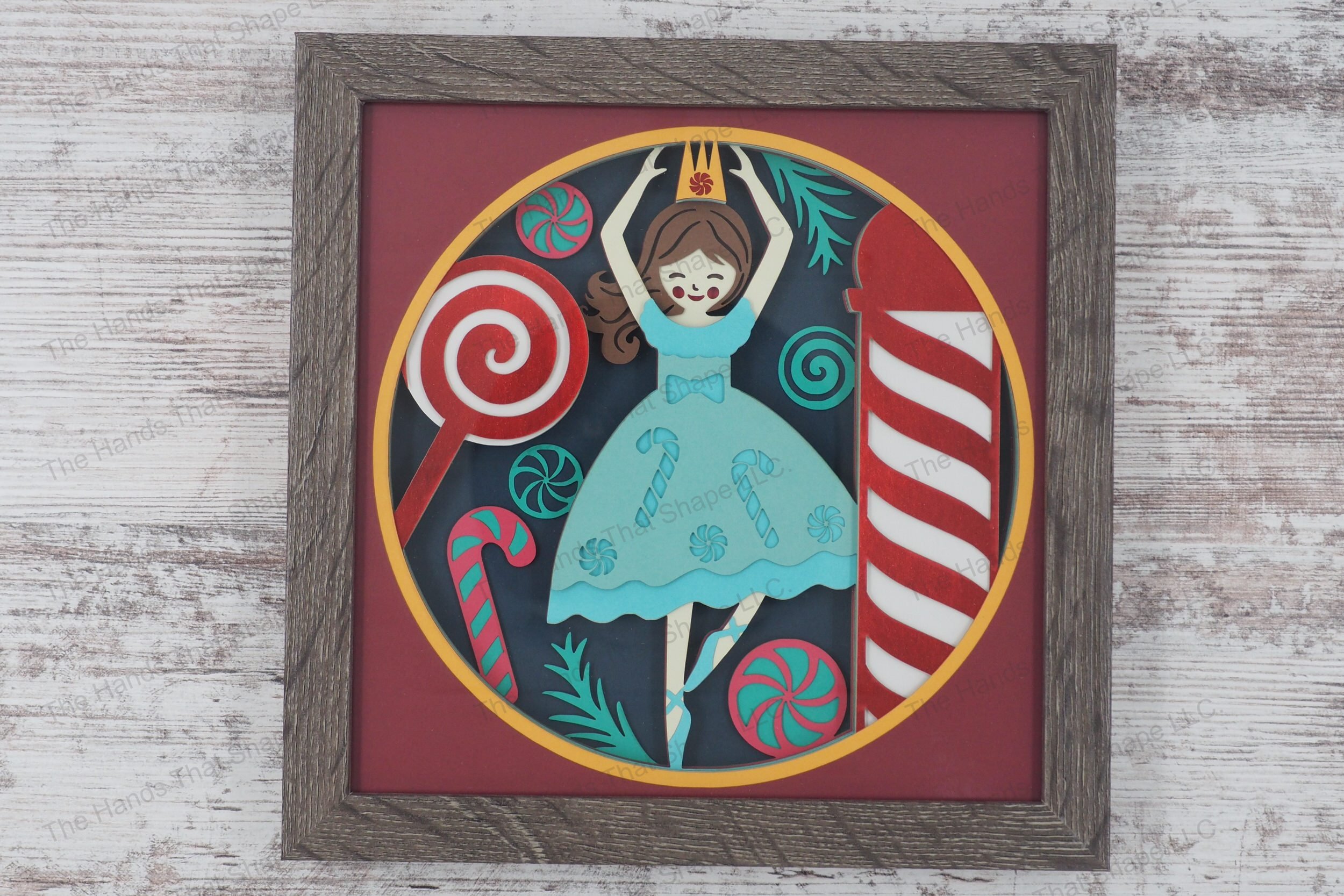 A whimsical framed layered paper shadowbox depicting a Nutcracker-inspired ballerina with a candy-themed dress, surrounded by pinwheels and candy canes.