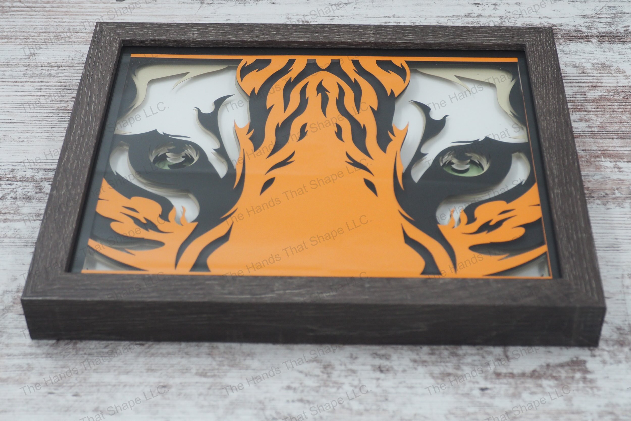 A framed layered paper shadowbox capturing the intense gaze of a tiger's eyes, crafted from 7 layers of cardstock, creating depth and a 3D effect.