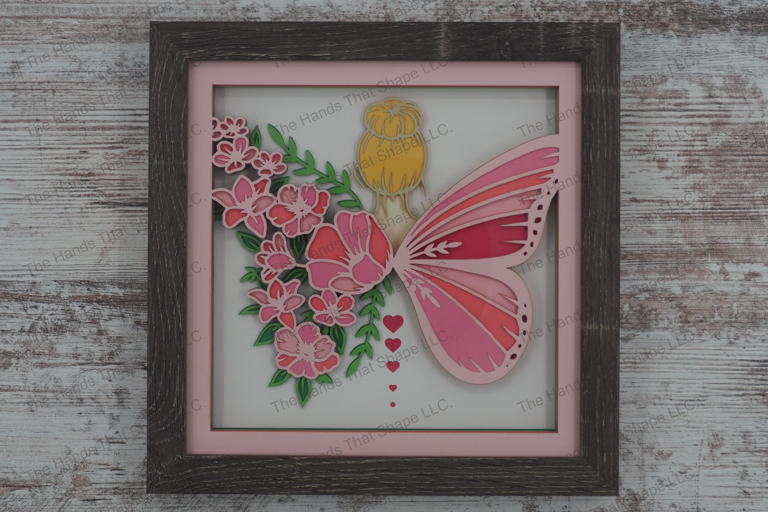 A layered paper shadowbox depicting a forest fairy with one butterfly wing and another made of flowers, crafted from 12 layers of cardstock in a gray MDF frame.