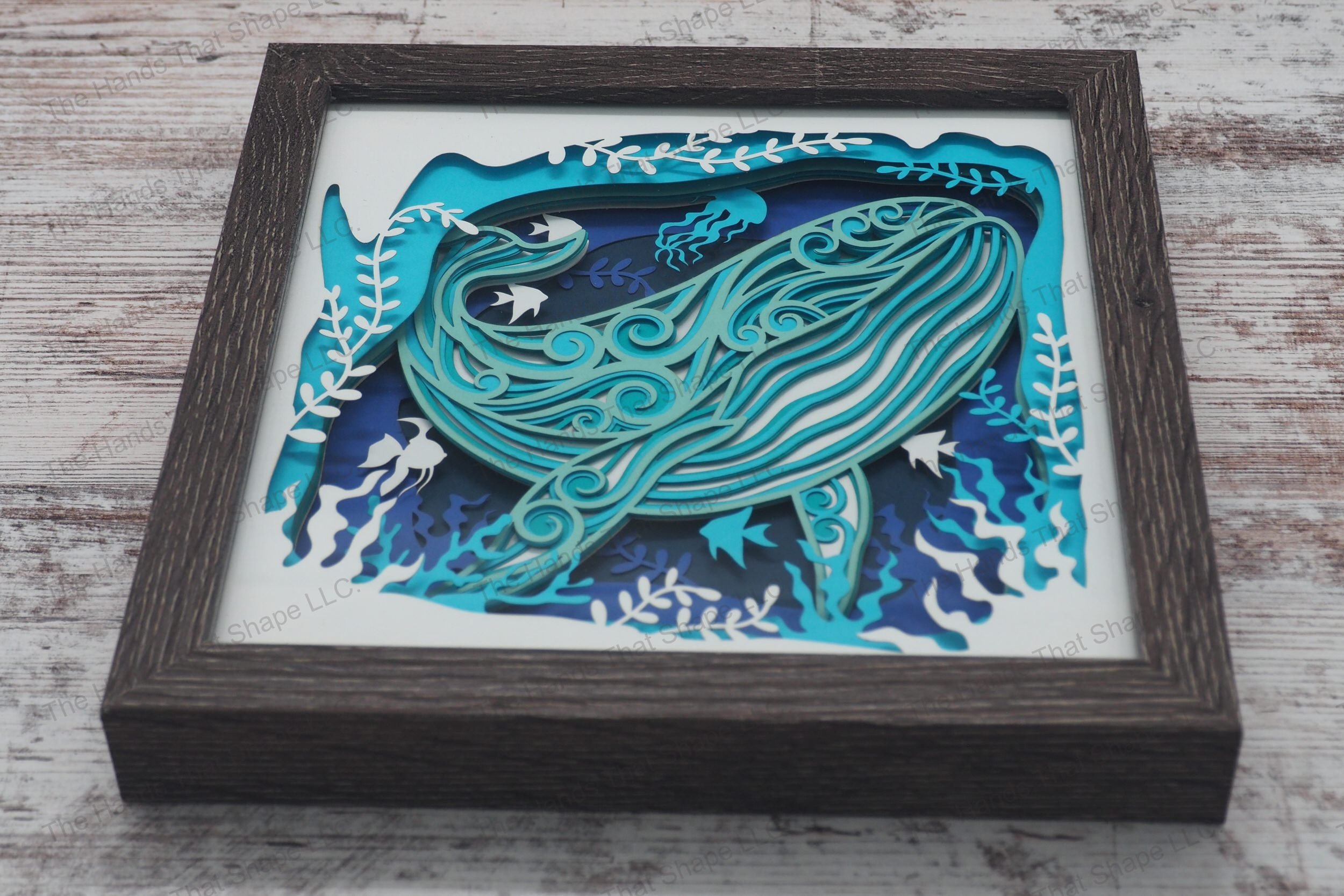A layered paper shadowbox depicting a vibrant underwater scene with a large whale surrounded by plants, fish, and jellyfish, crafted from 8 layers of cardstock.