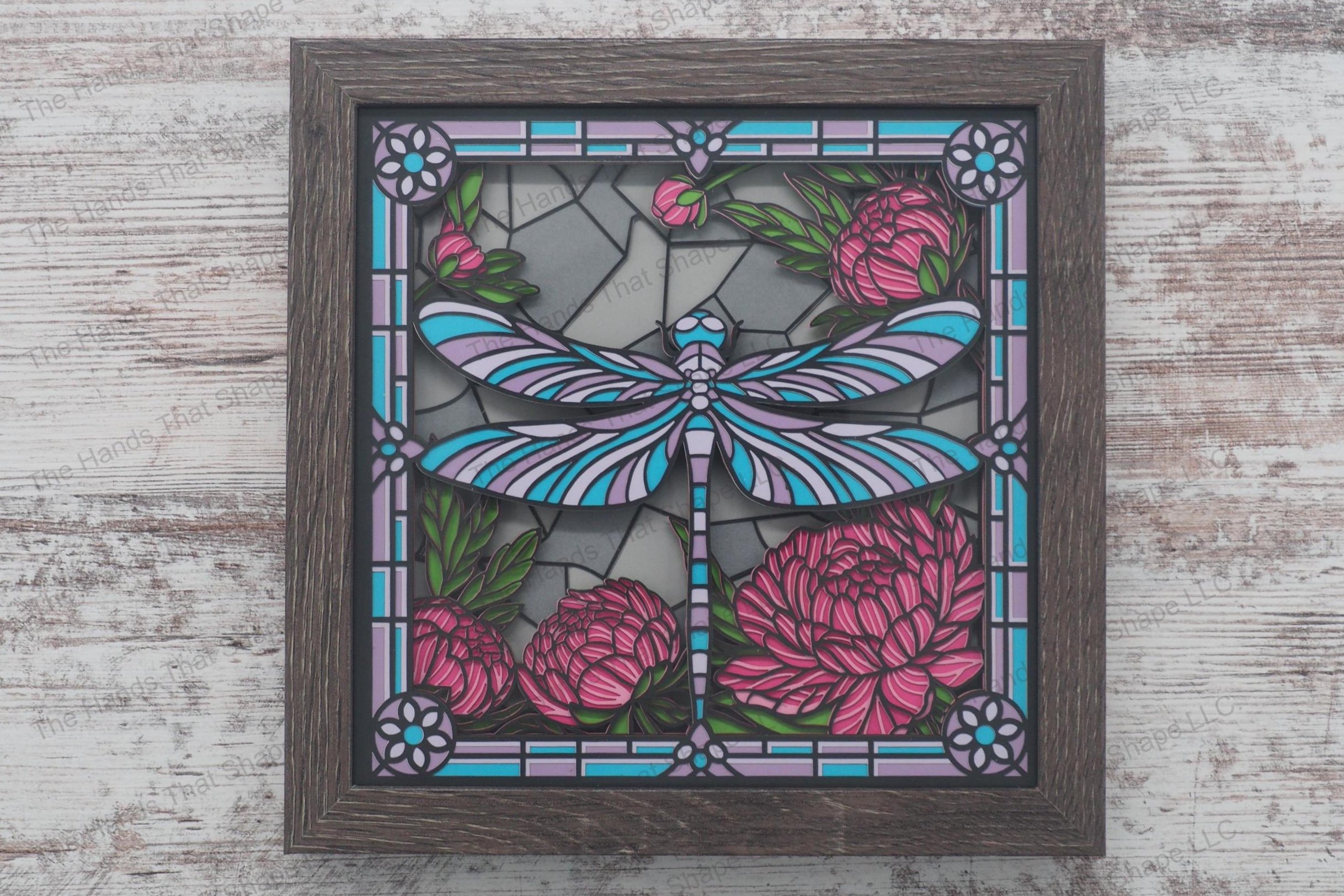 A framed layered paper shadowbox depicting a dragonfly hovering over a blooming garden, crafted in a stained glass style, made from 11 layers of cardstock.