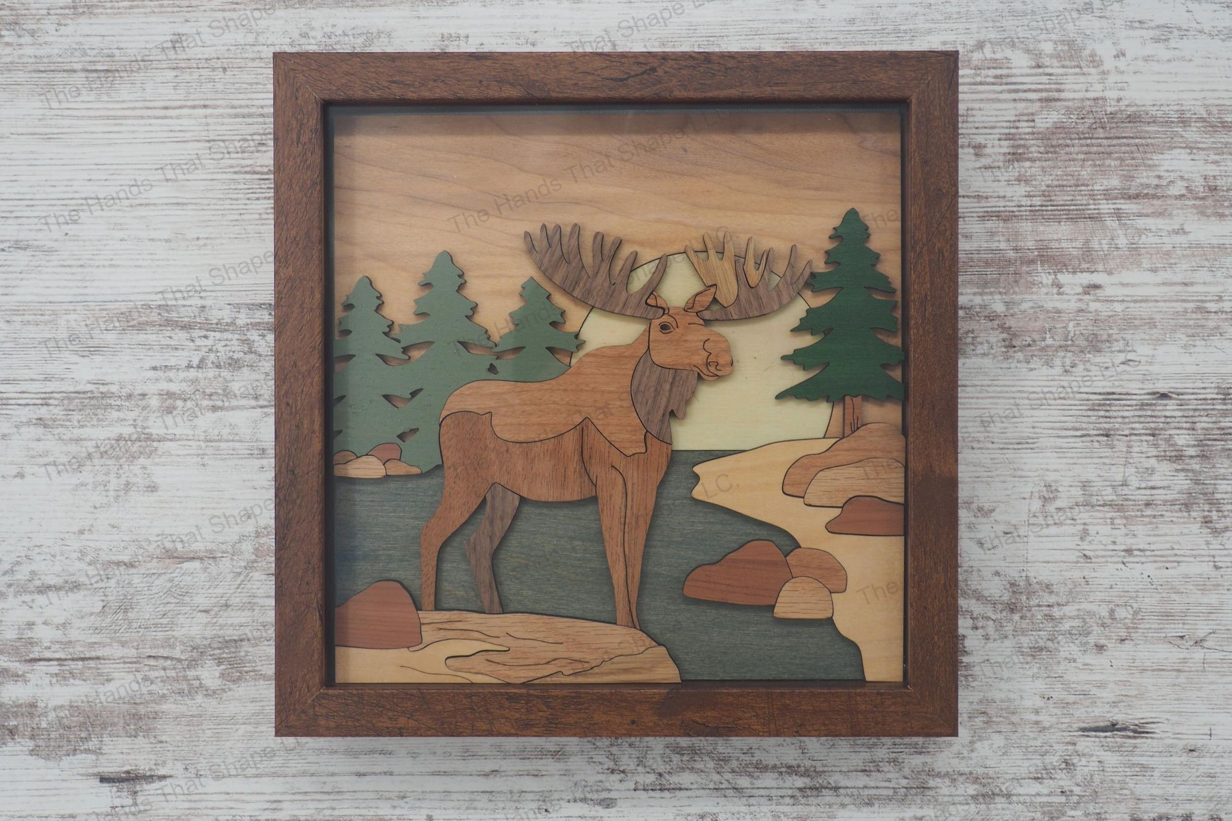Craft a stunning 3D inlay art piece with our laser-ready file featuring a majestic moose next to a stream, with a backdrop of pine trees and a setting sun.