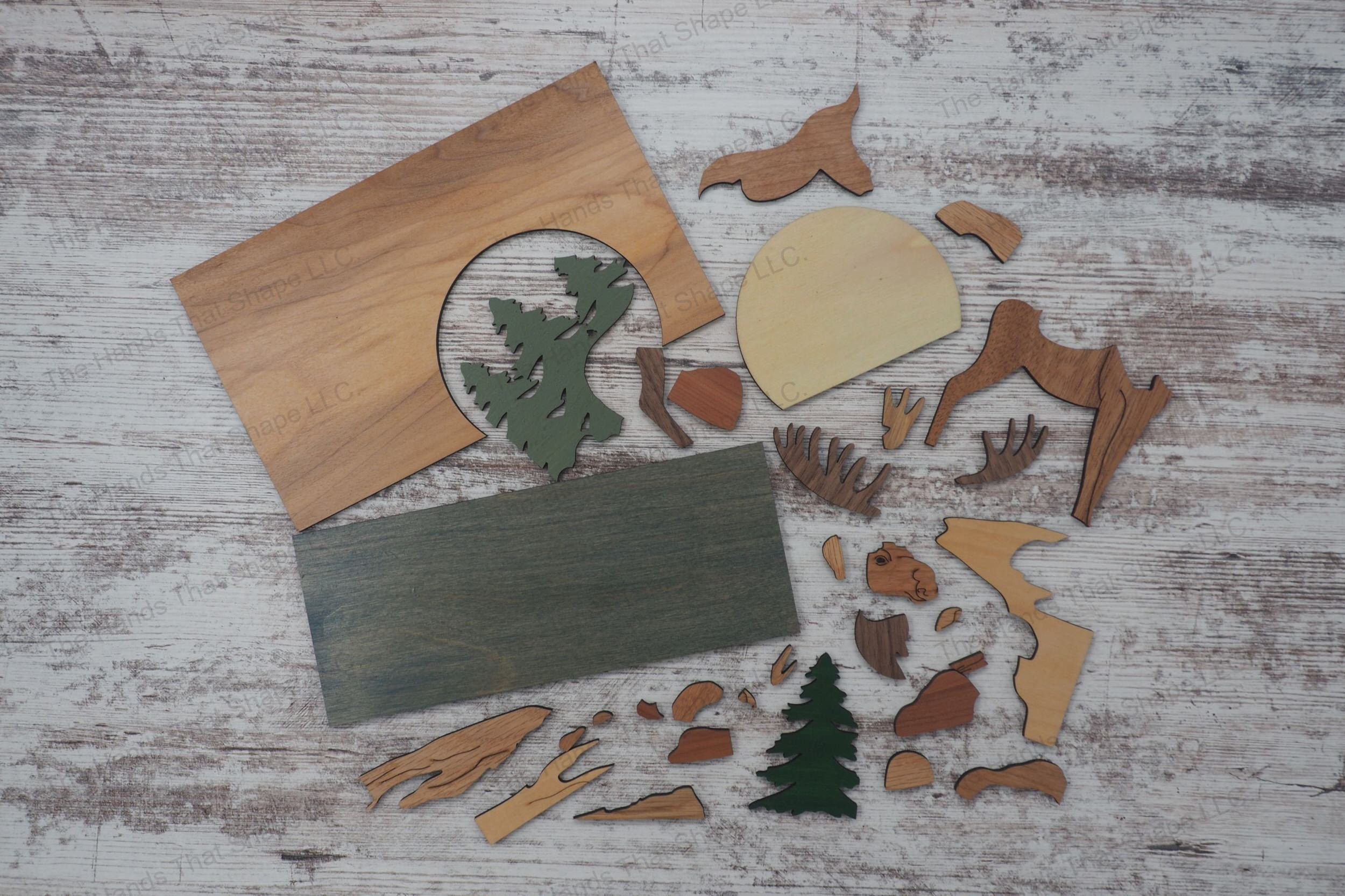 Craft a stunning 3D inlay art piece with our laser-ready file featuring a majestic moose next to a stream, with a backdrop of pine trees and a setting sun.