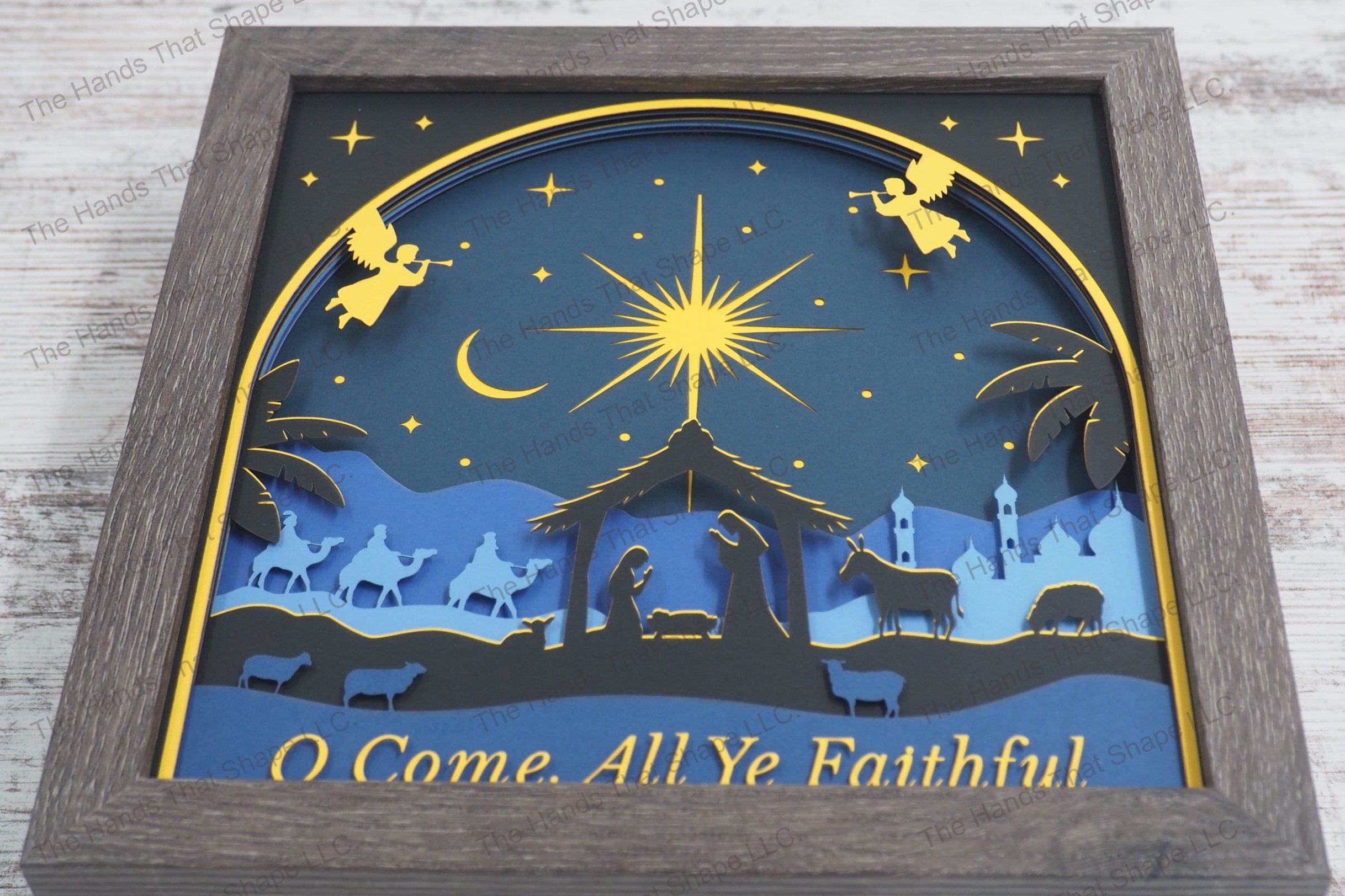 A detailed framed layered paper shadowbox depicting the nativity scene with silhouettes of the Holy Family, animals, wise men, and celestial angels.